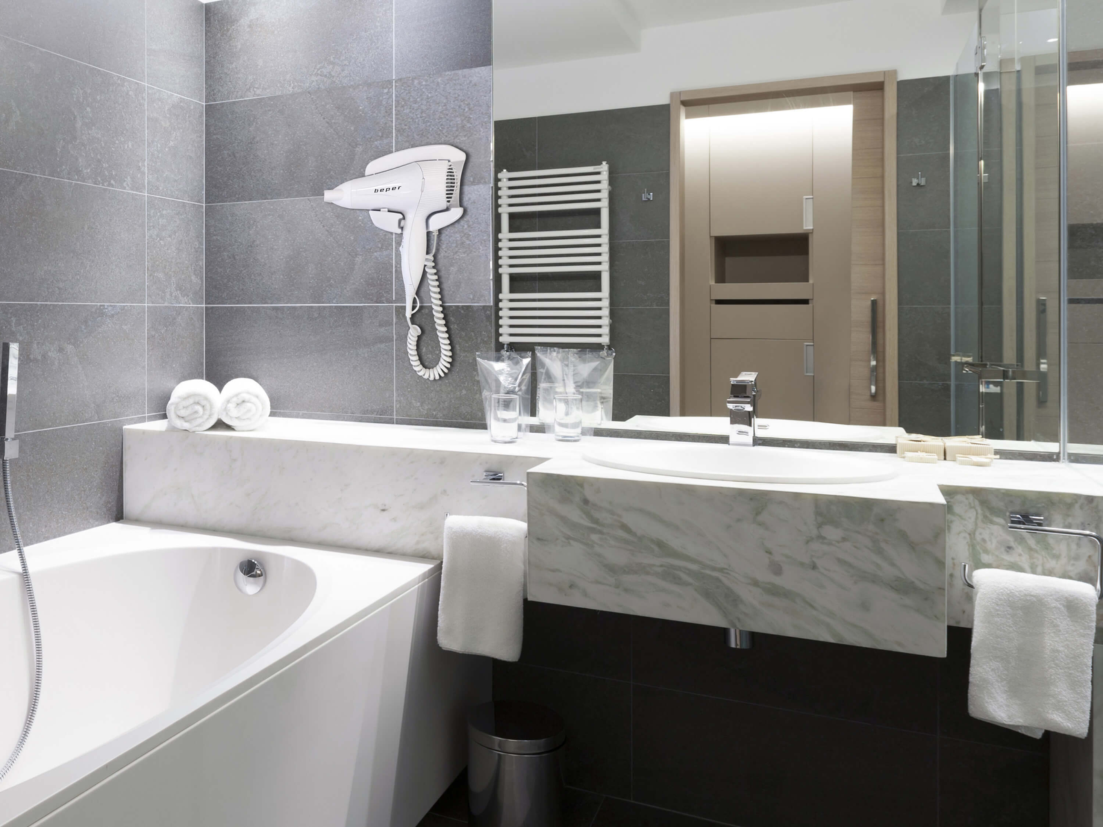 Modernes Badezimmer mit Badewanne, Waschbecken, Spiegel und Föhn.