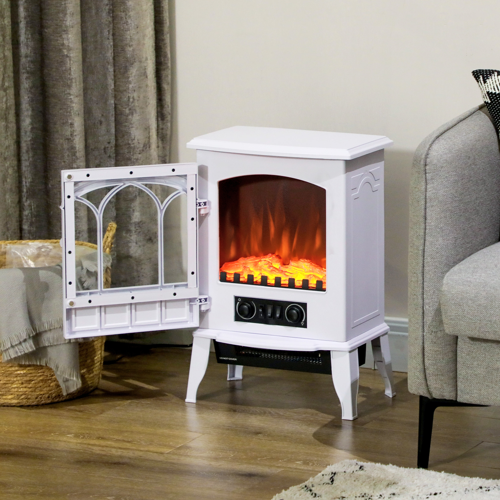 Caminetto elettrico bianco con porta aperta, mostra fiamme finte. Su pavimento in legno vicino divano.