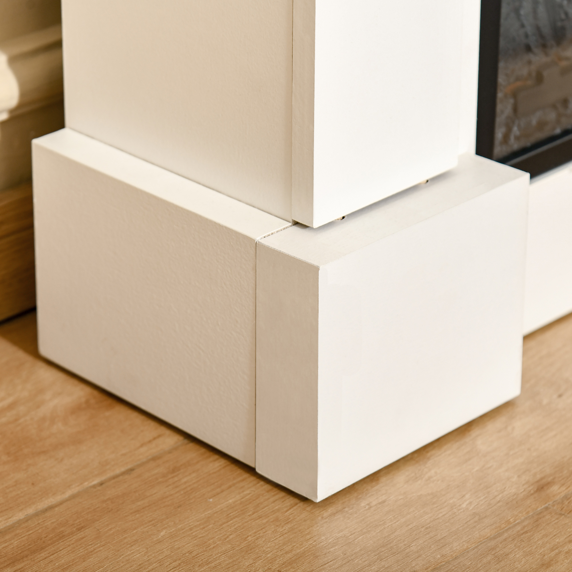 Base de chimenea rectangular blanca con un suelo de madera natural. La chimenea está al fondo.
