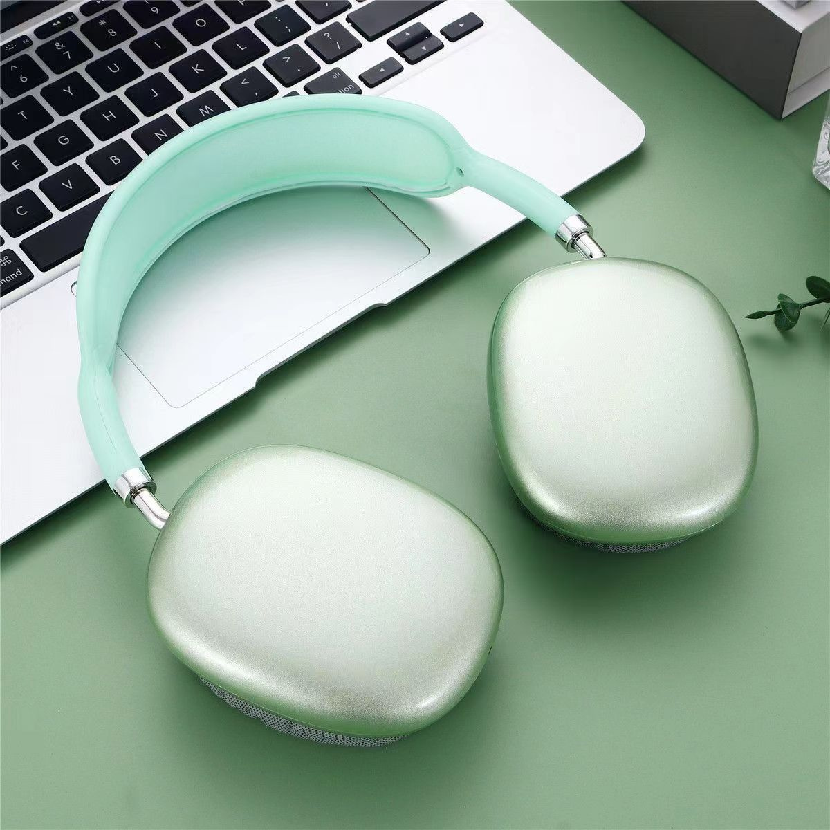 Kopfhörer mit mintgrünem Bügel und Ohrmuscheln, auf Laptop-Tastatur und grüner Oberfläche.