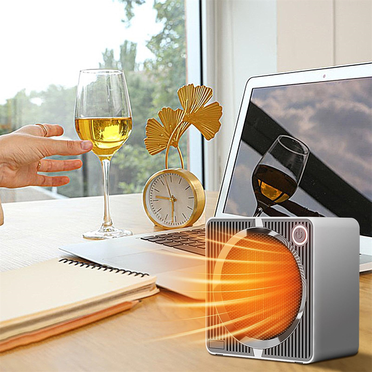 Ein kleiner Heizlüfter gibt Wärme in Richtung eines Tisches mit Laptop, Weinglas und Uhr ab. Eine Hand greift nach dem Weinglas.