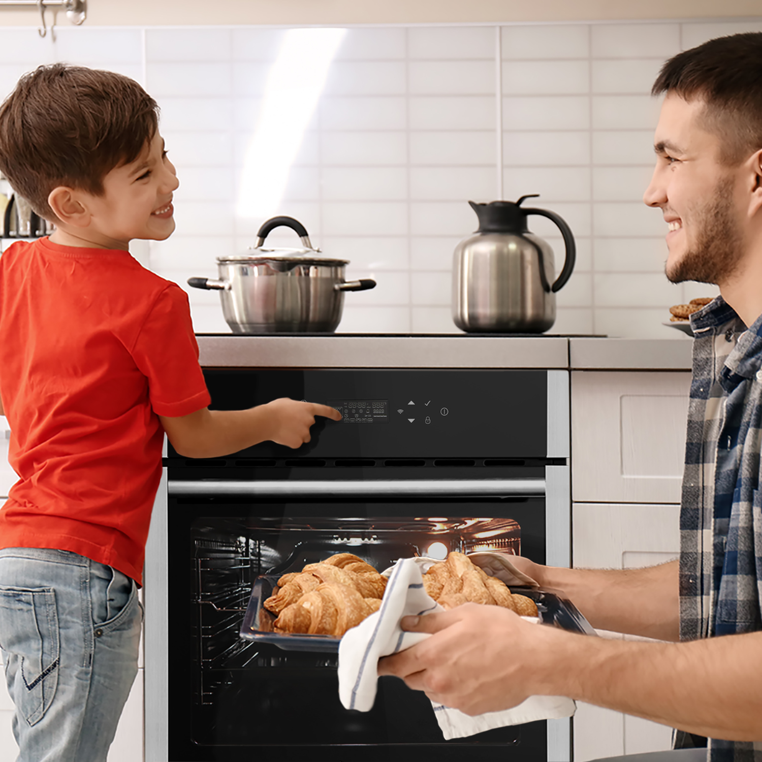 Ein Vater und sein Sohn nehmen ein Tablett mit Croissants aus einem Ofen. Die Backofentür ist offen.