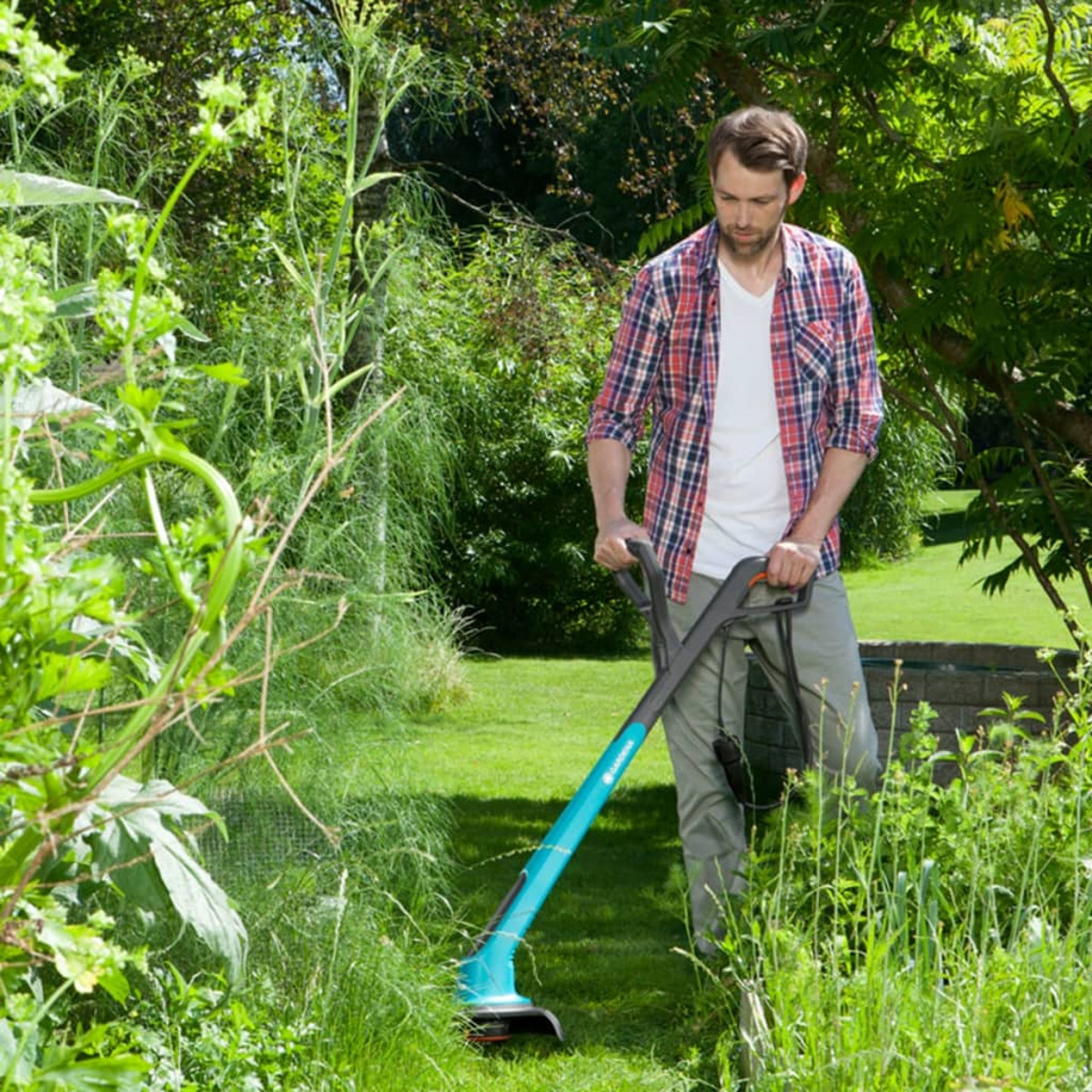 Mann benutzt Rasentrimmer in einem Garten mit grünem Gras und Pflanzen.