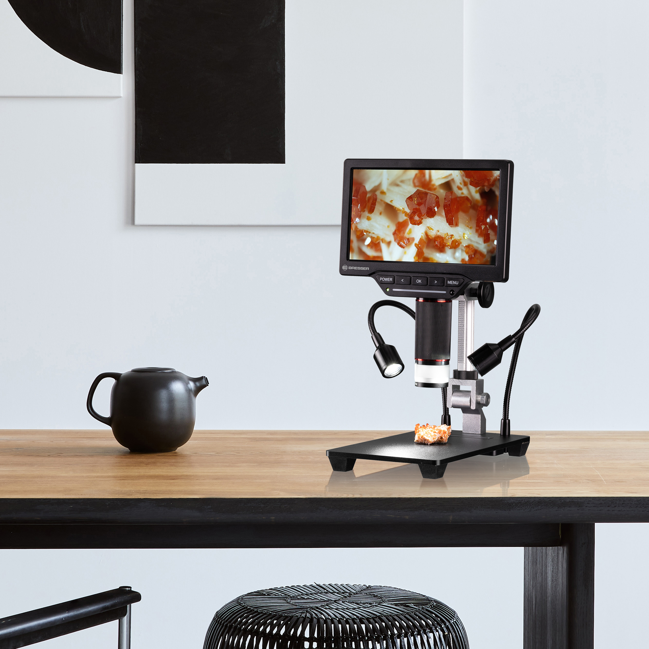 Configuración de microscopio en mesa de madera con muestra pequeña y pantalla con vista ampliada.