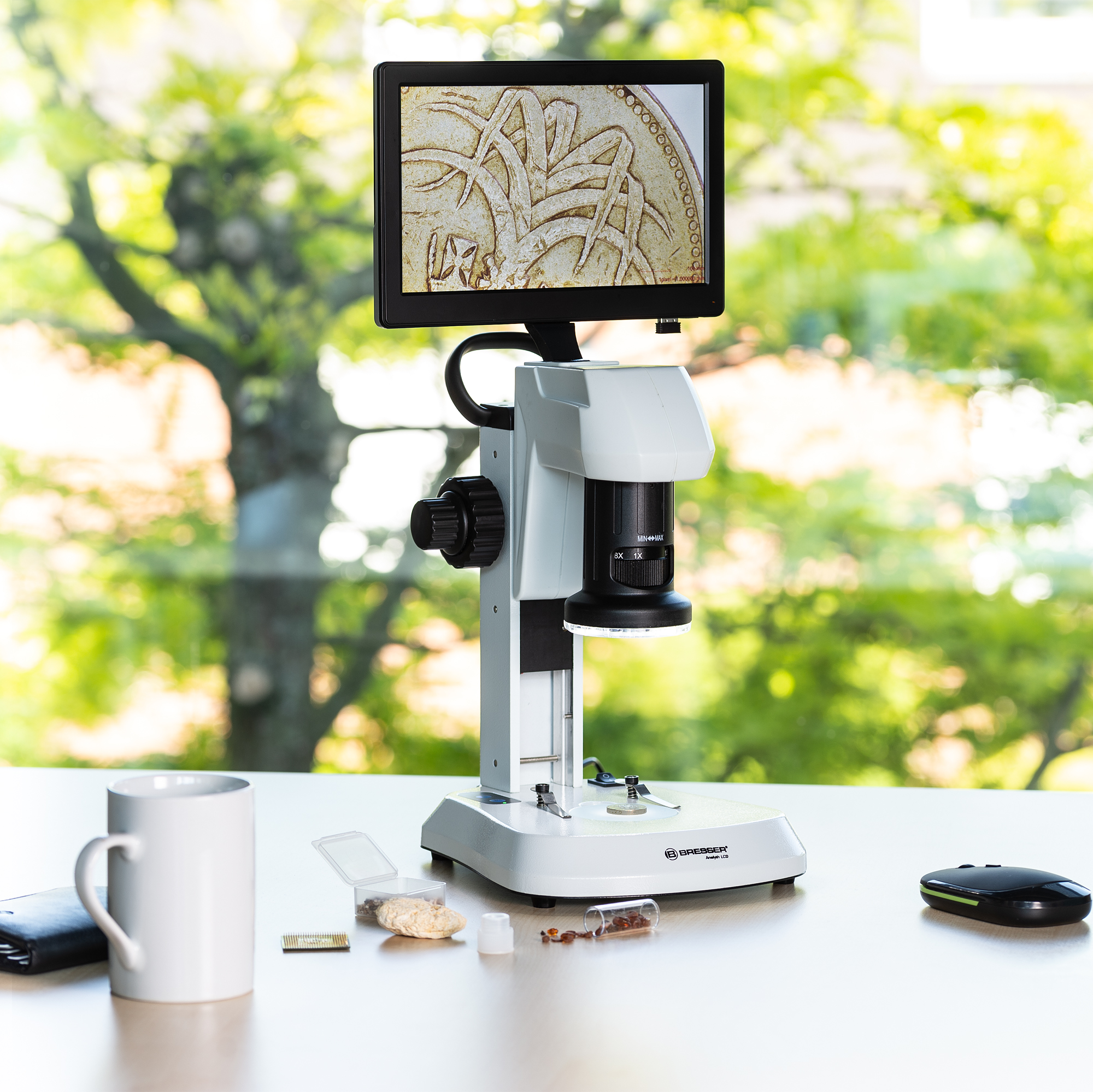 Un microscopio blanco con una pantalla, una taza blanca y otras herramientas de laboratorio sobre una mesa blanca.
