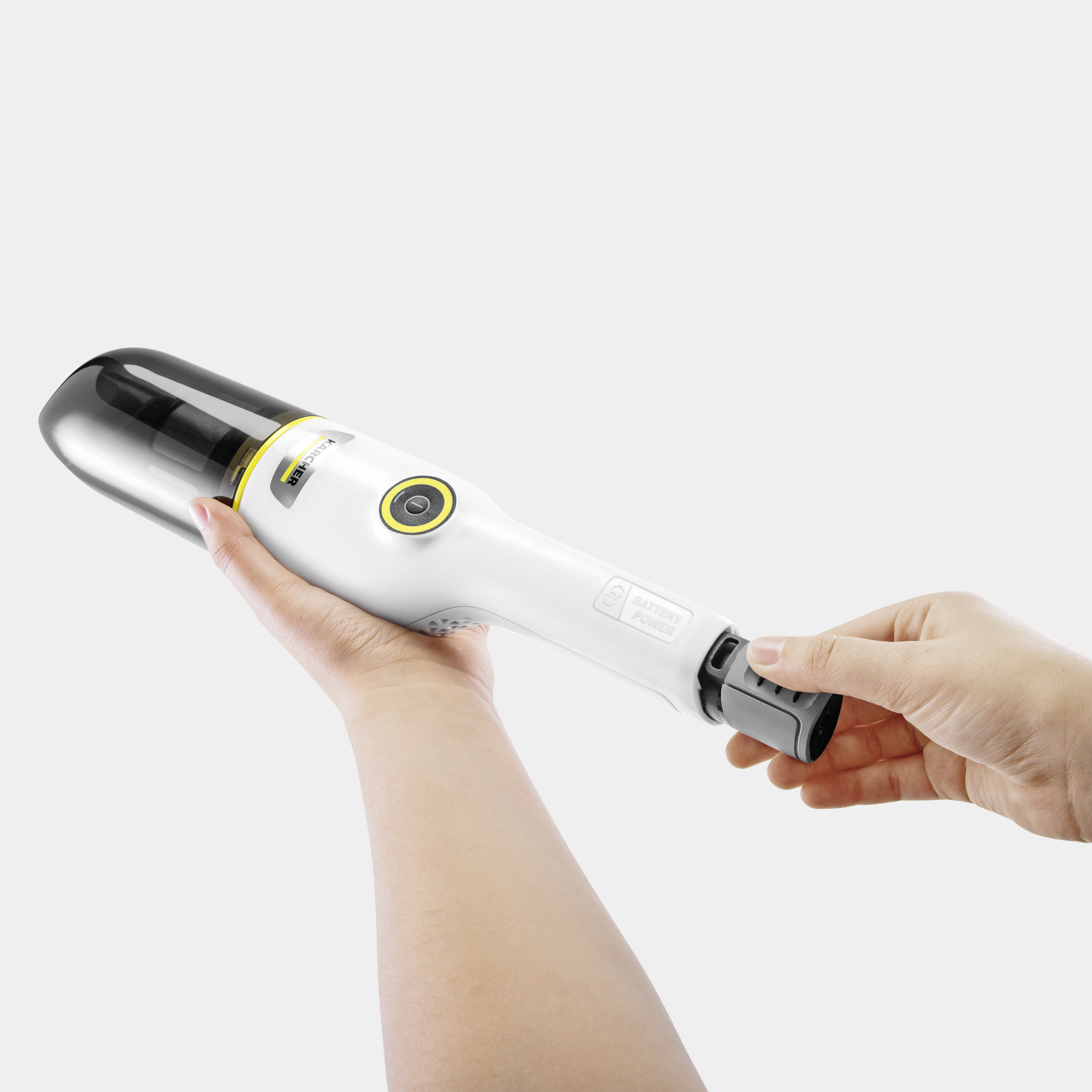 Hand holding a white and yellow handheld vacuum cleaner. The power button is visible and a black cap is present.