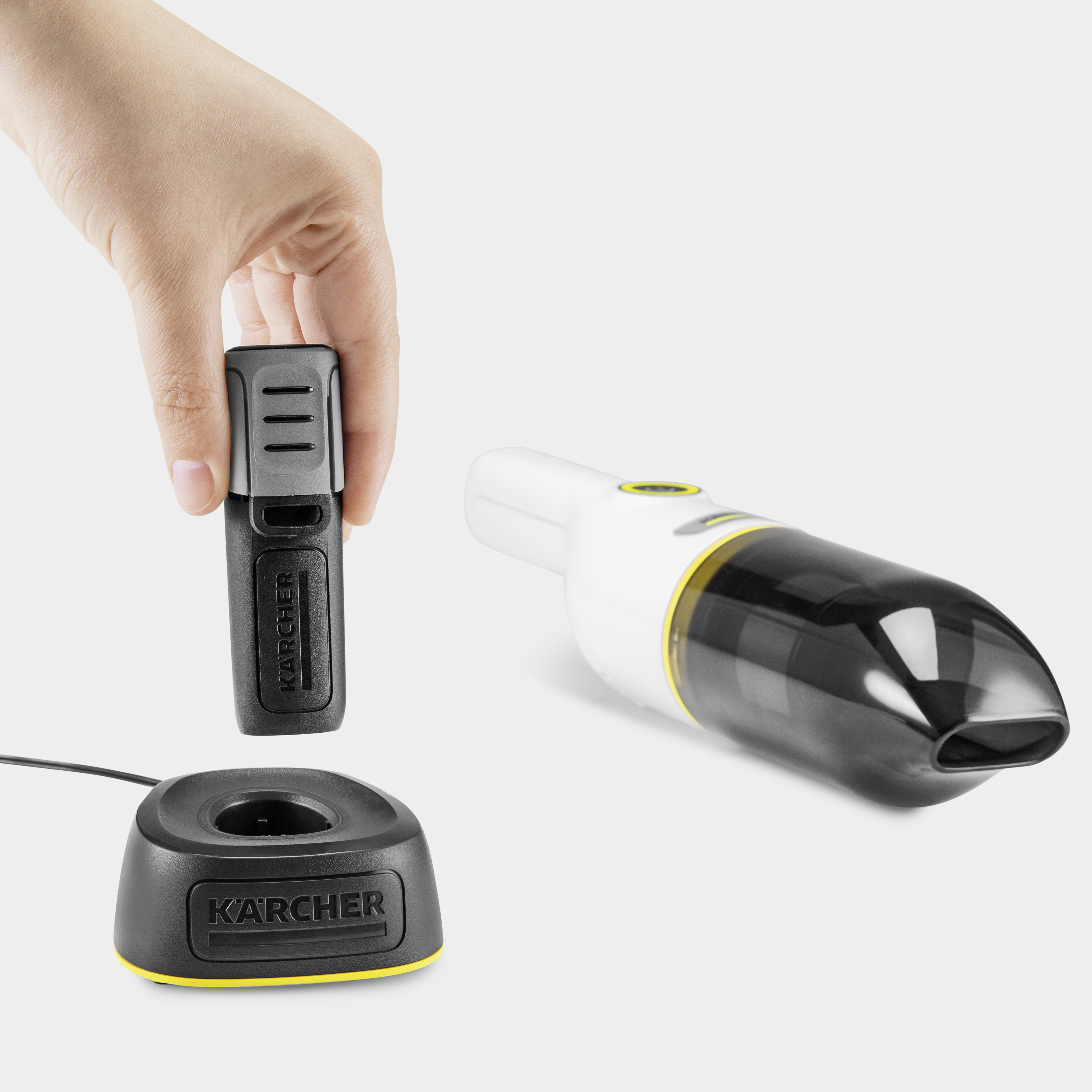 Hand holding a black and white handheld vacuum with a charging base.