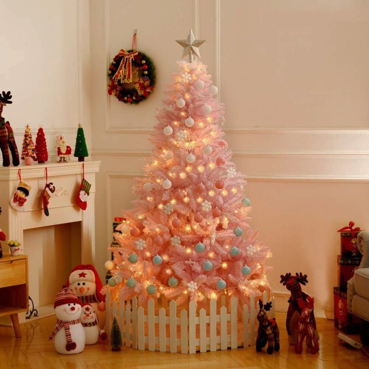 Árbol de Navidad rosa decorado con luces y adornos en una habitación. Un muñeco de nieve está en frente.