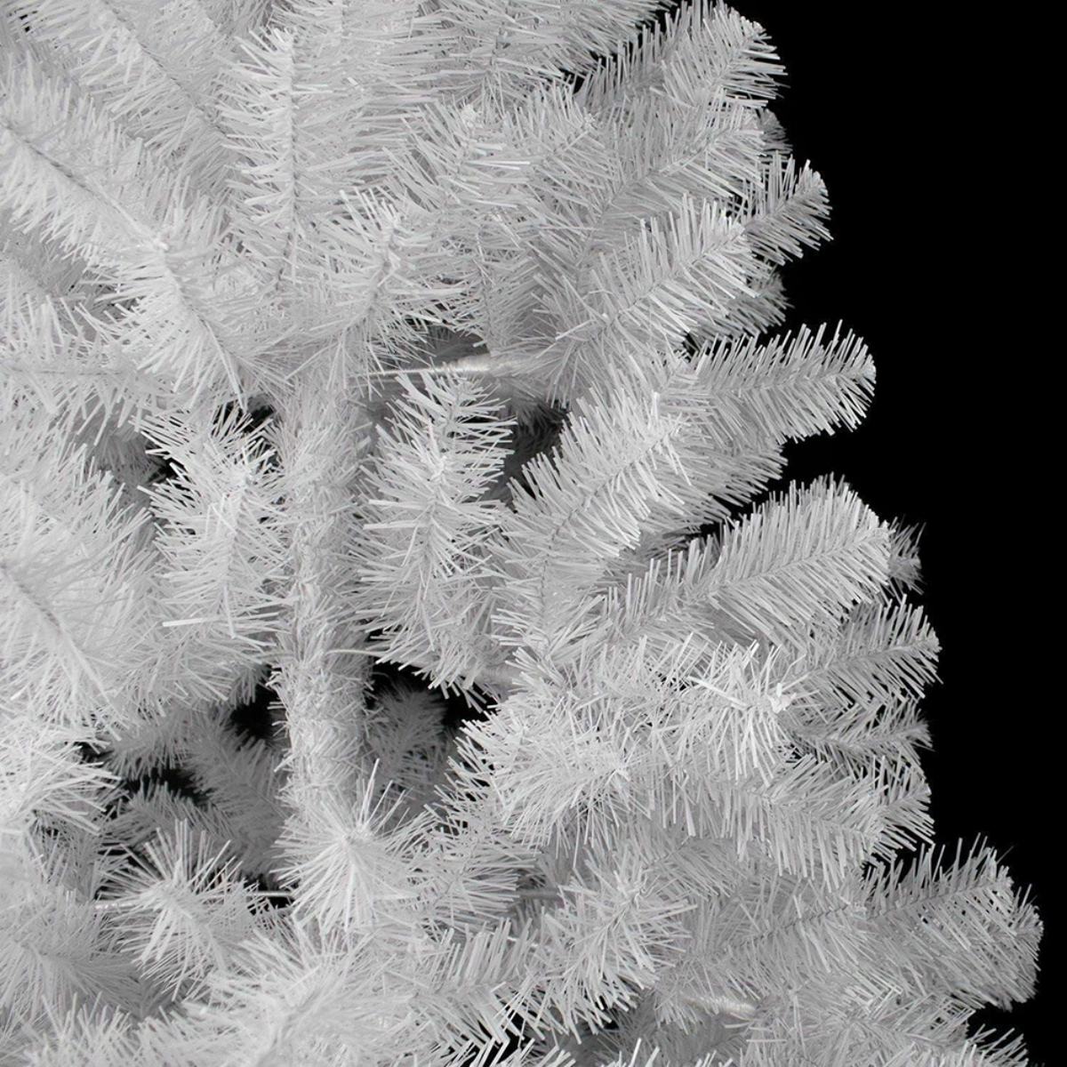 Primer plano de un árbol de Navidad artificial blanco con muchas agujas, sobre fondo negro.