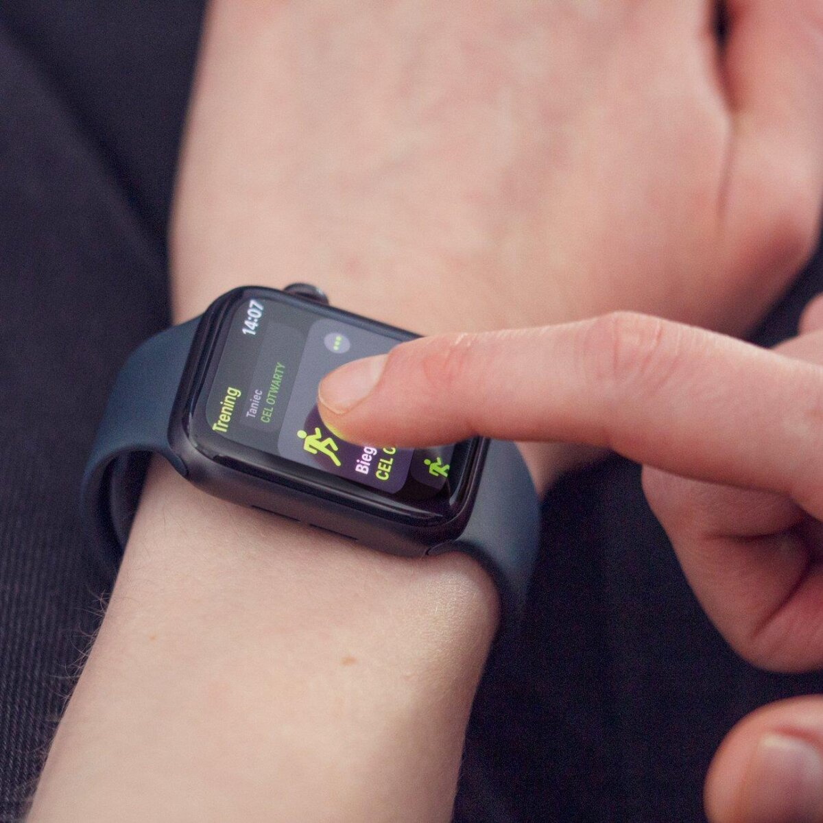 Handgelenk einer Person mit Smartwatch, die eine App-Oberfläche anzeigt, ein Finger berührt den Bildschirm.