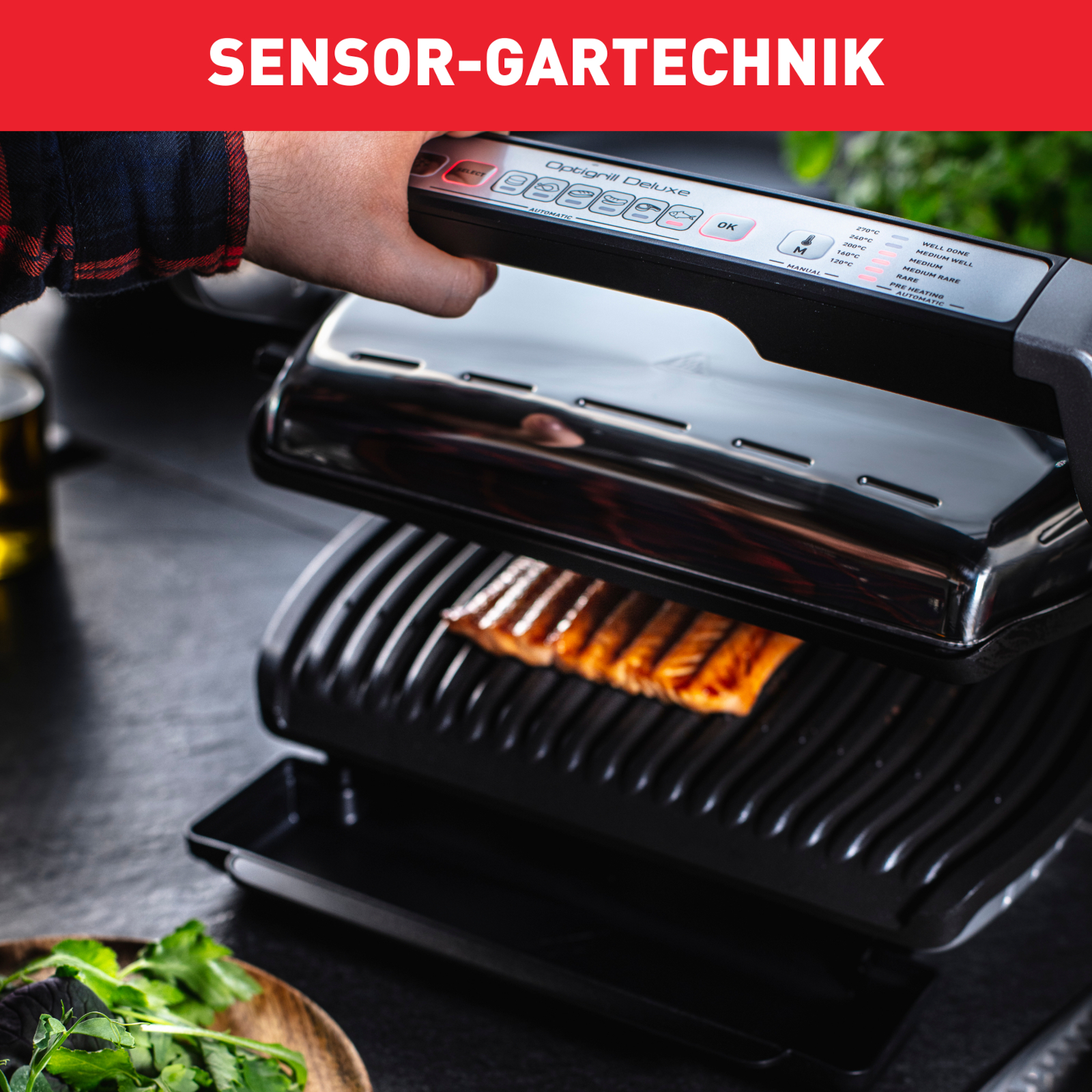 Czarny grill z dłonią obsługującą go. Jedzenie się grilluje. Zielone liście na stole.