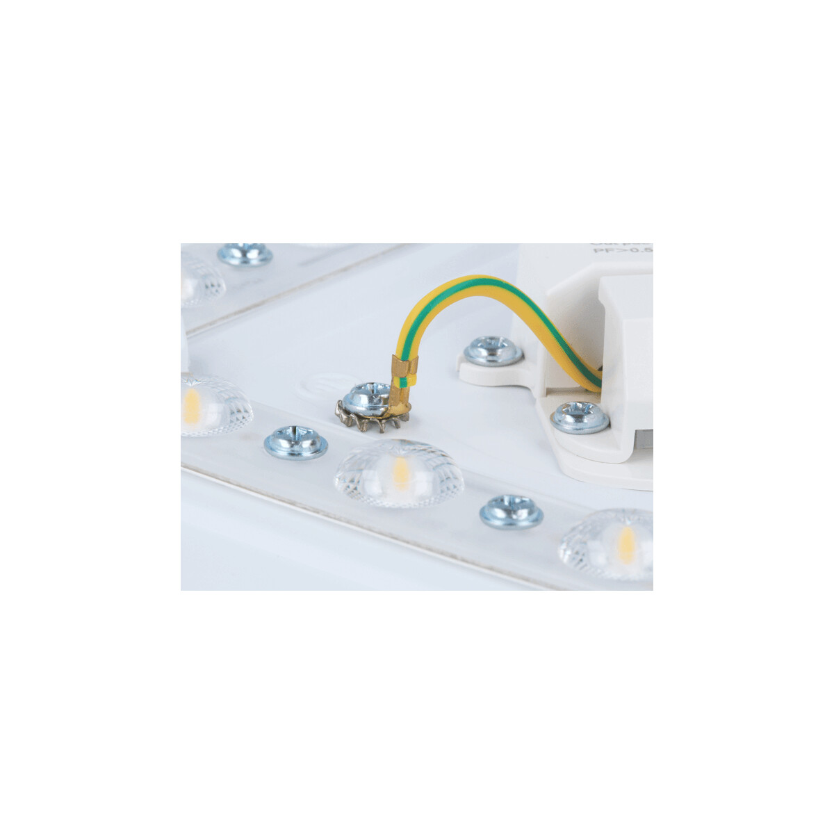 Nahaufnahme einer weißen elektrischen Komponente mit Schrauben, einem gelb-grünen Draht und LED-Leuchten. Details sind sichtbar.