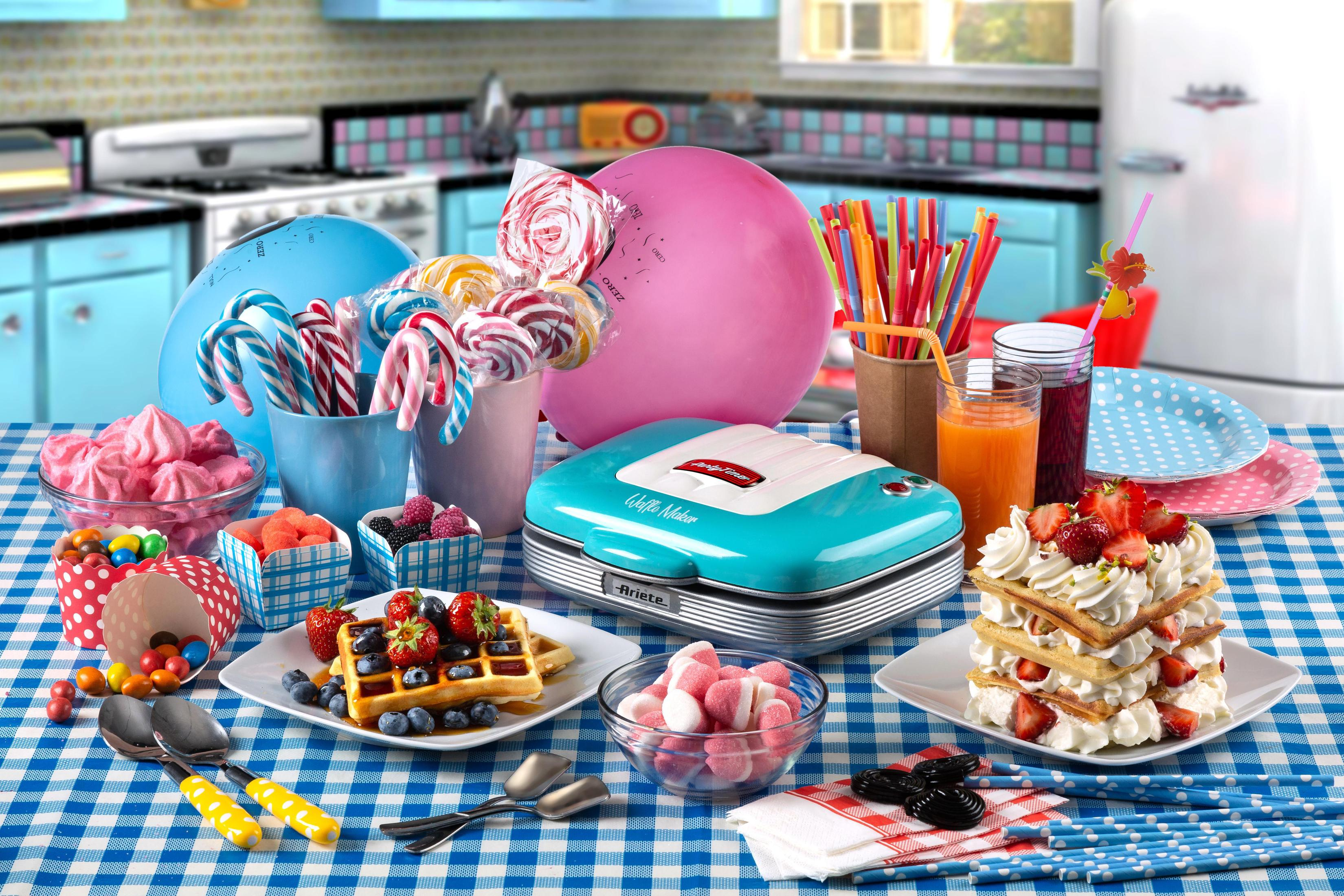 Tafel met diverse zoetigheden en een wafelijzer. Kleurrijke lolly's, snoepjes en wafels zijn aanwezig.