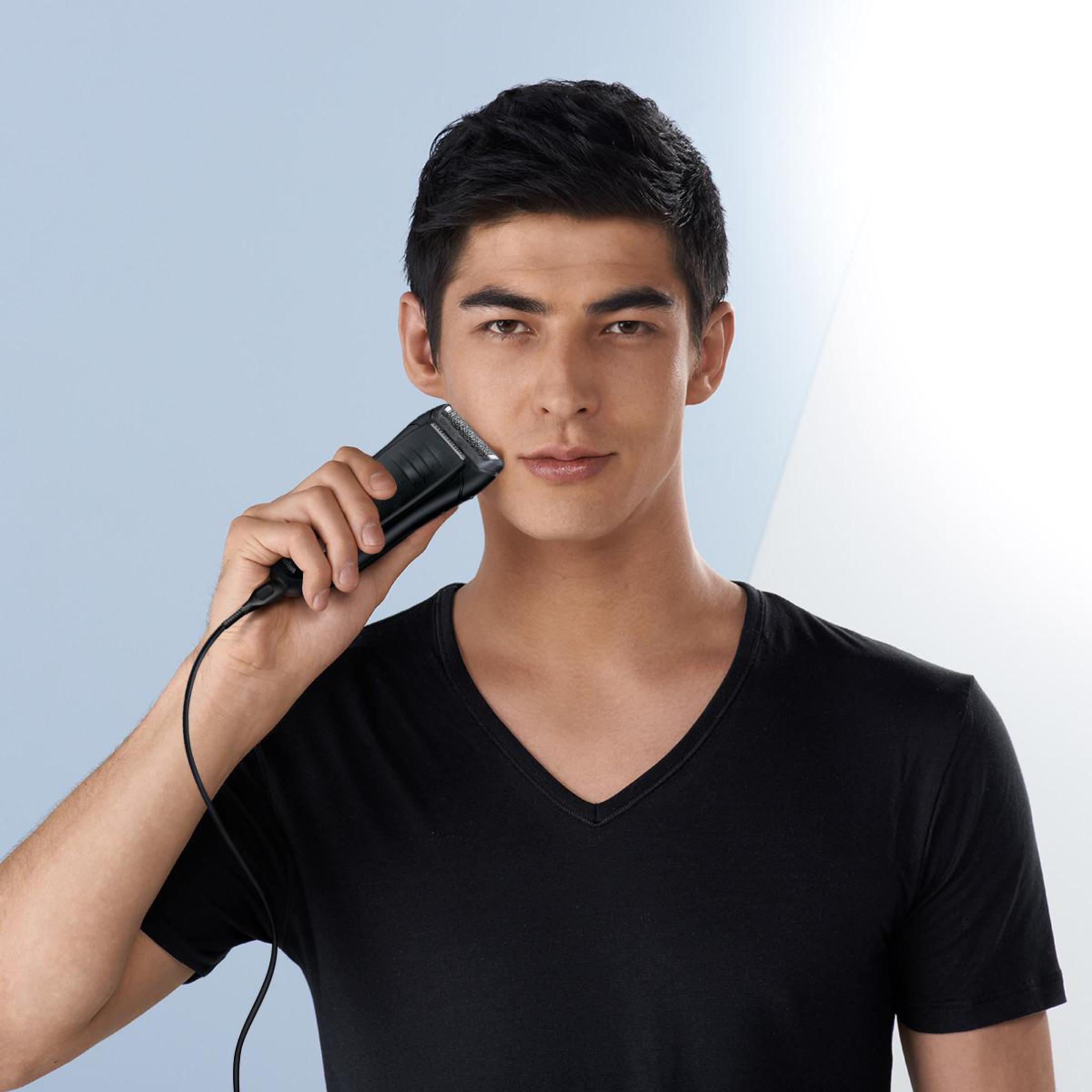 Ein Mann rasiert sich mit einem schwarzen Elektrorasierer. Er trägt ein schwarzes Hemd, der Hintergrund ist hellblau.