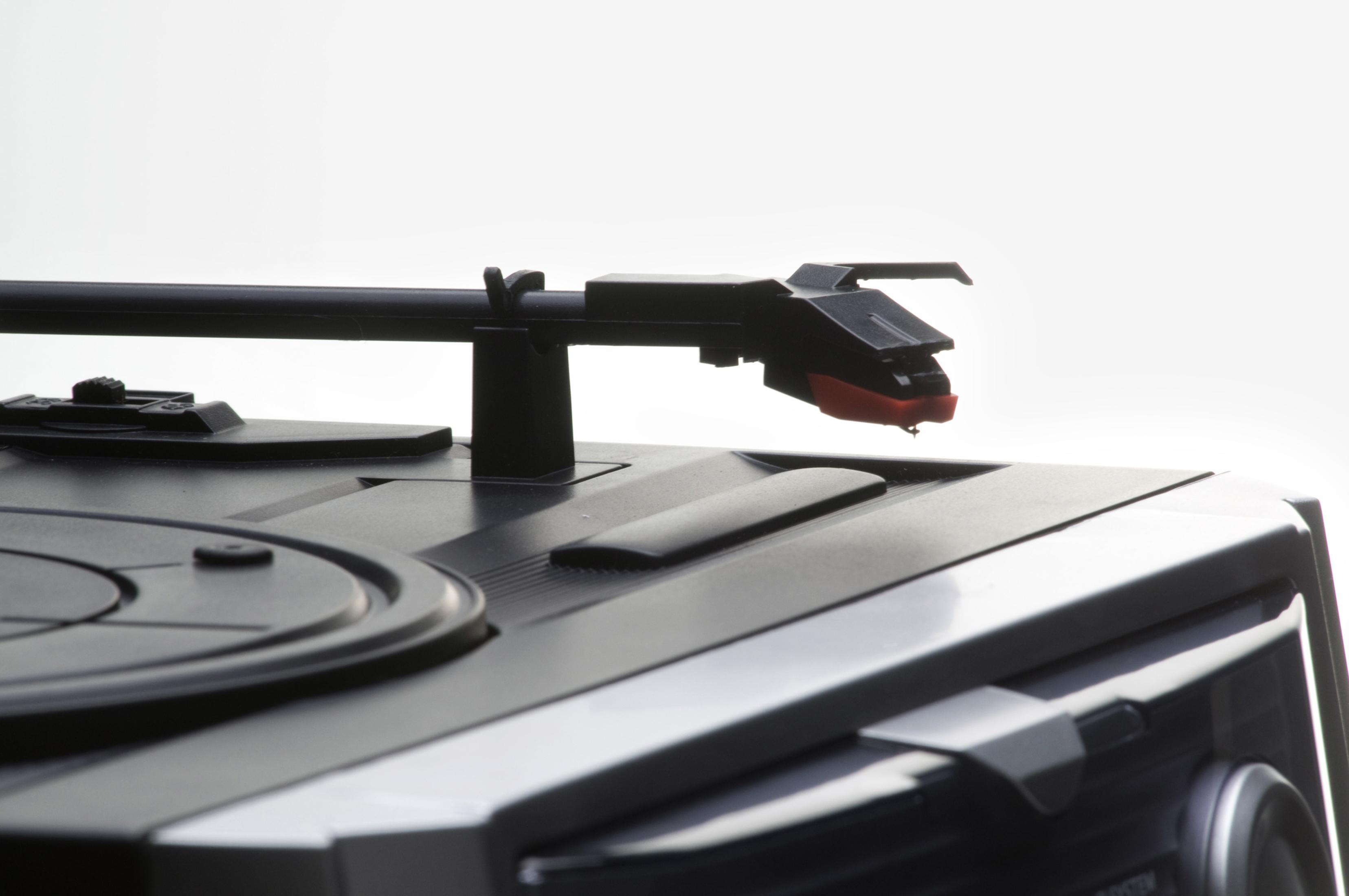 Plattenspielerkopf und Arm über einem schwarzen Stereo-System. Der Kopf hat eine rote Nadel.