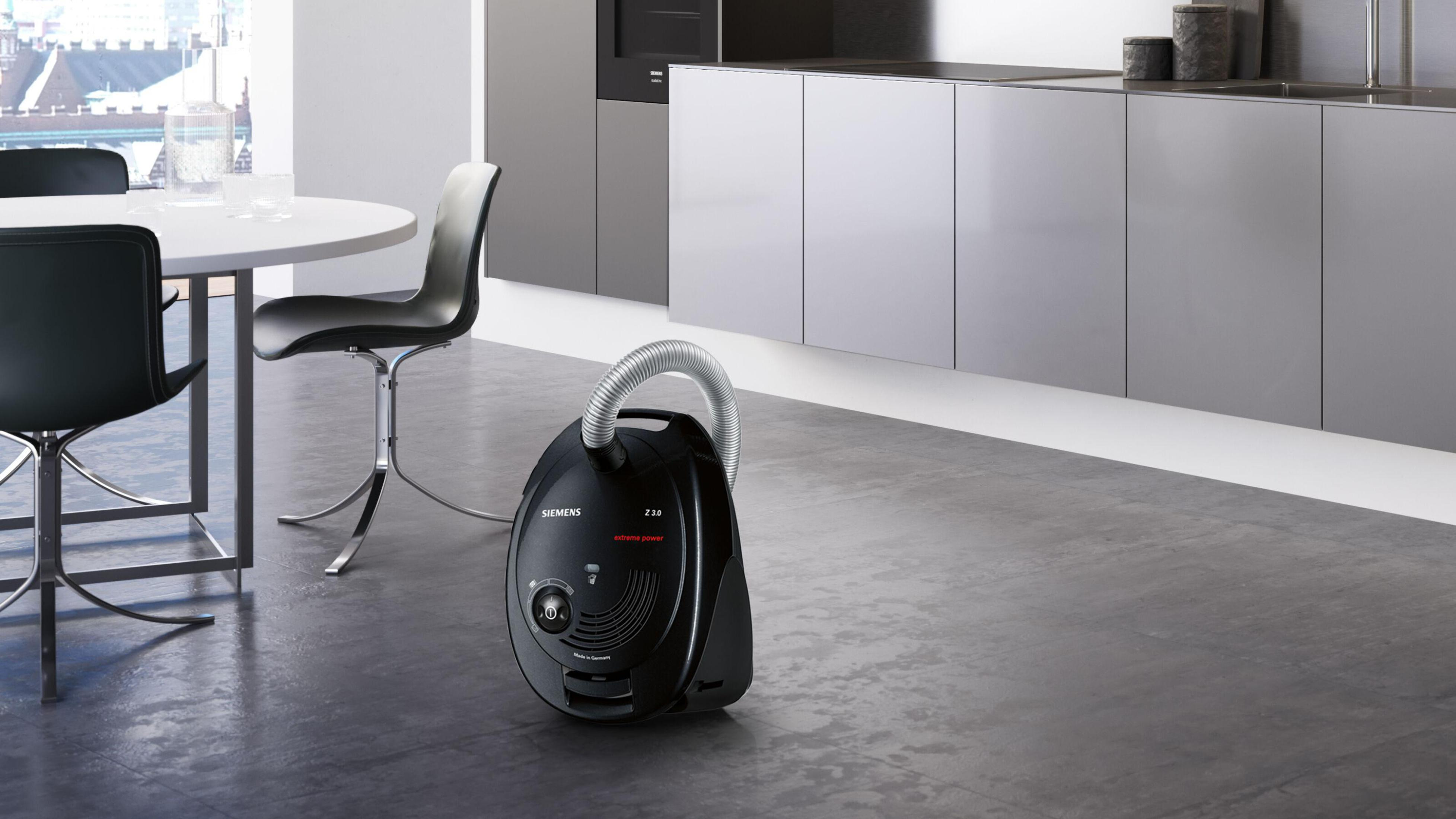 Czarny odkurzacz na szarej podłodze w nowoczesnej kuchni. Tło obejmuje stół i szafki.