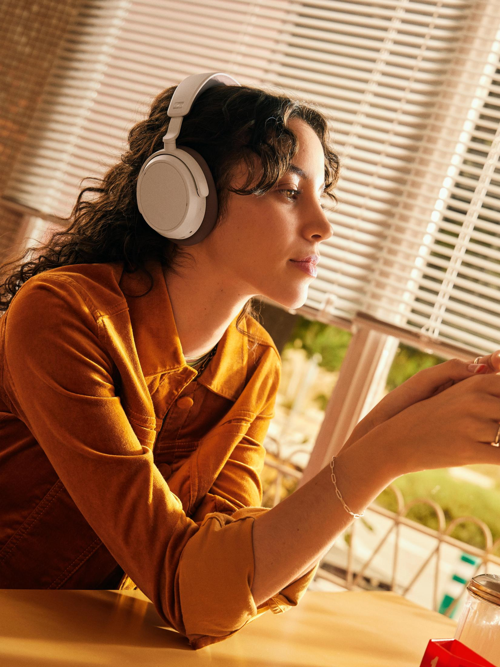 Kobieta w białych słuchawkach patrzy na komputer. Ma kręcone włosy i się uśmiecha.