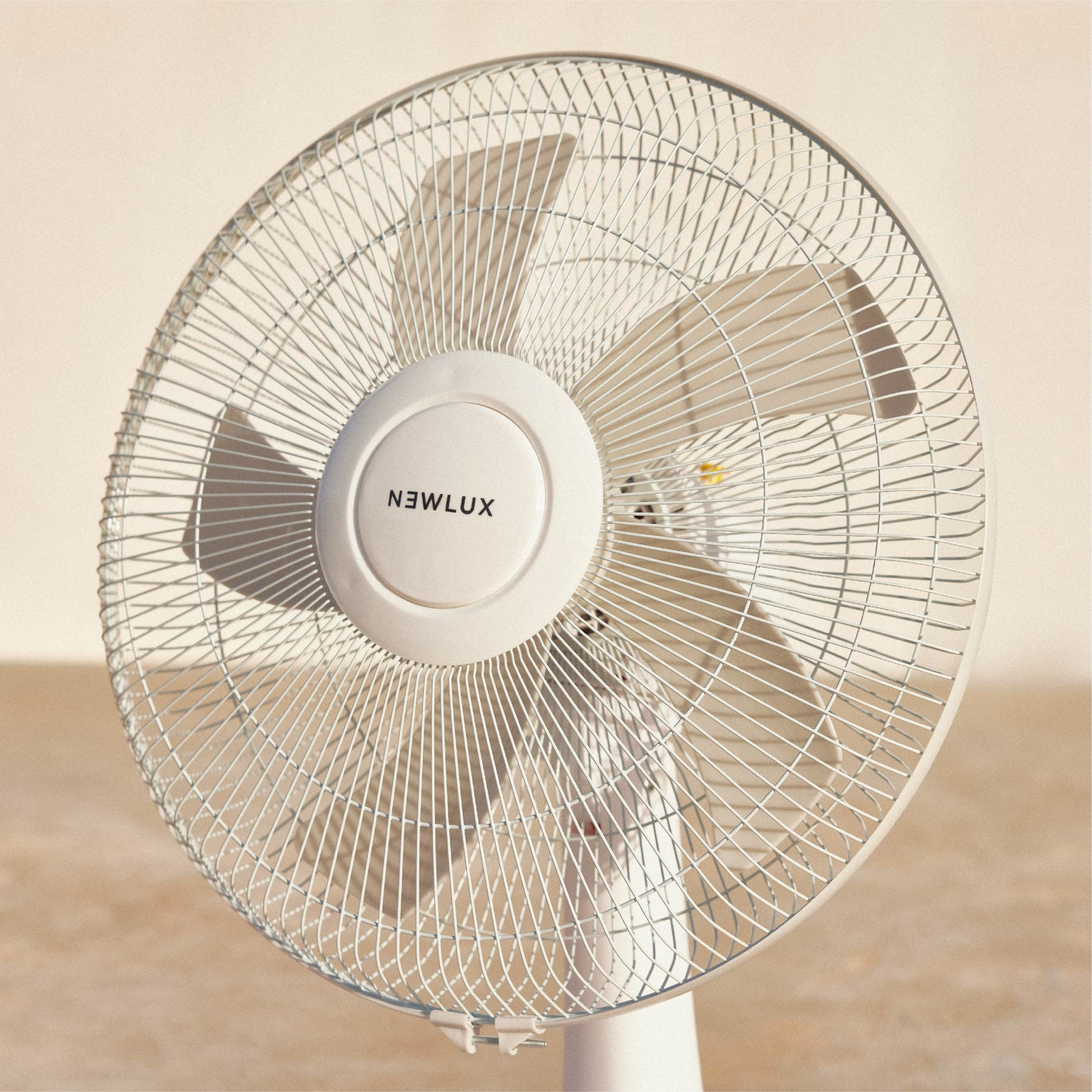 Ventilador eléctrico blanco con tres aspas, base y rejilla protectora blancas.