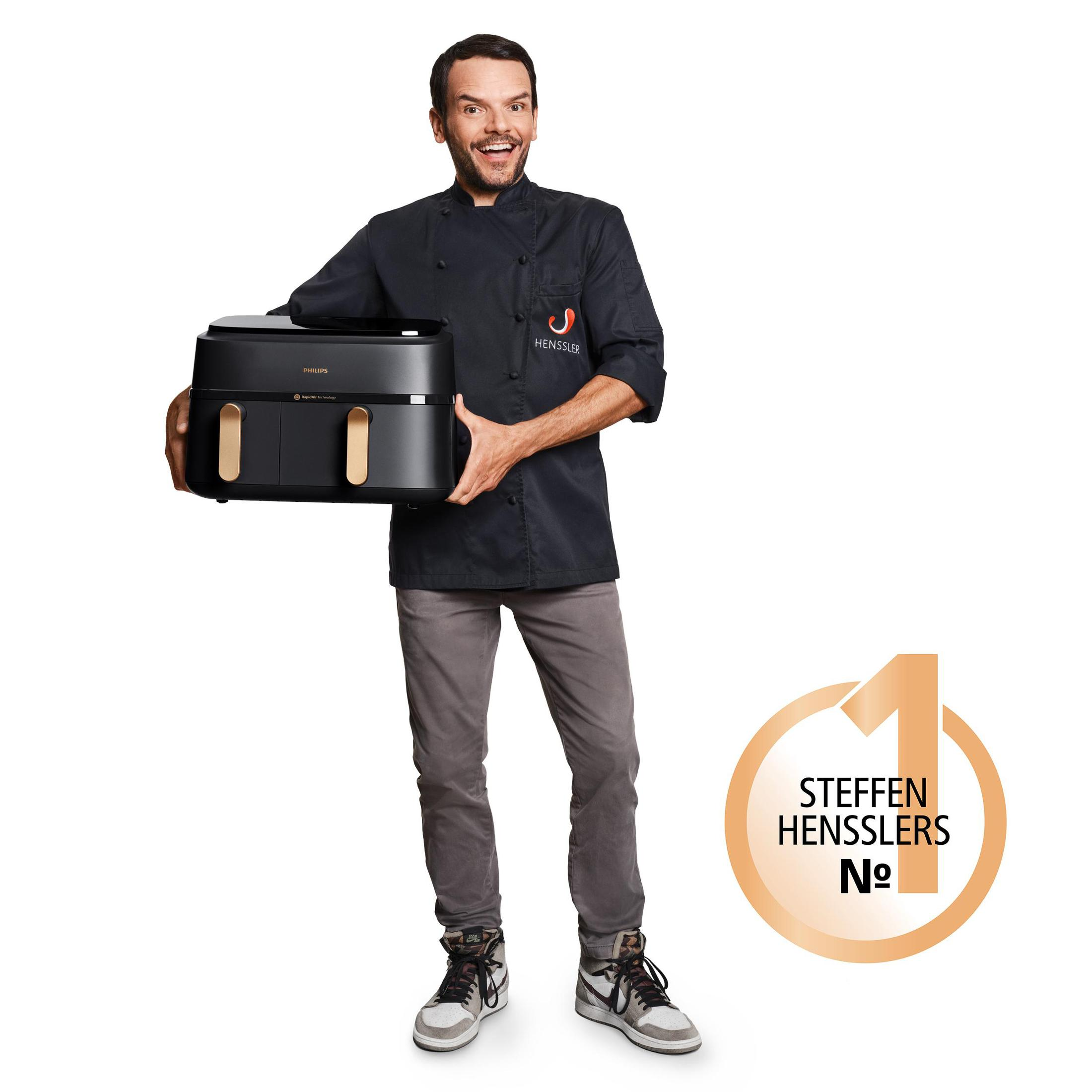 Un homme en veste de chef noire tient une friteuse à air noire. Un logo avec '1' est à droite.