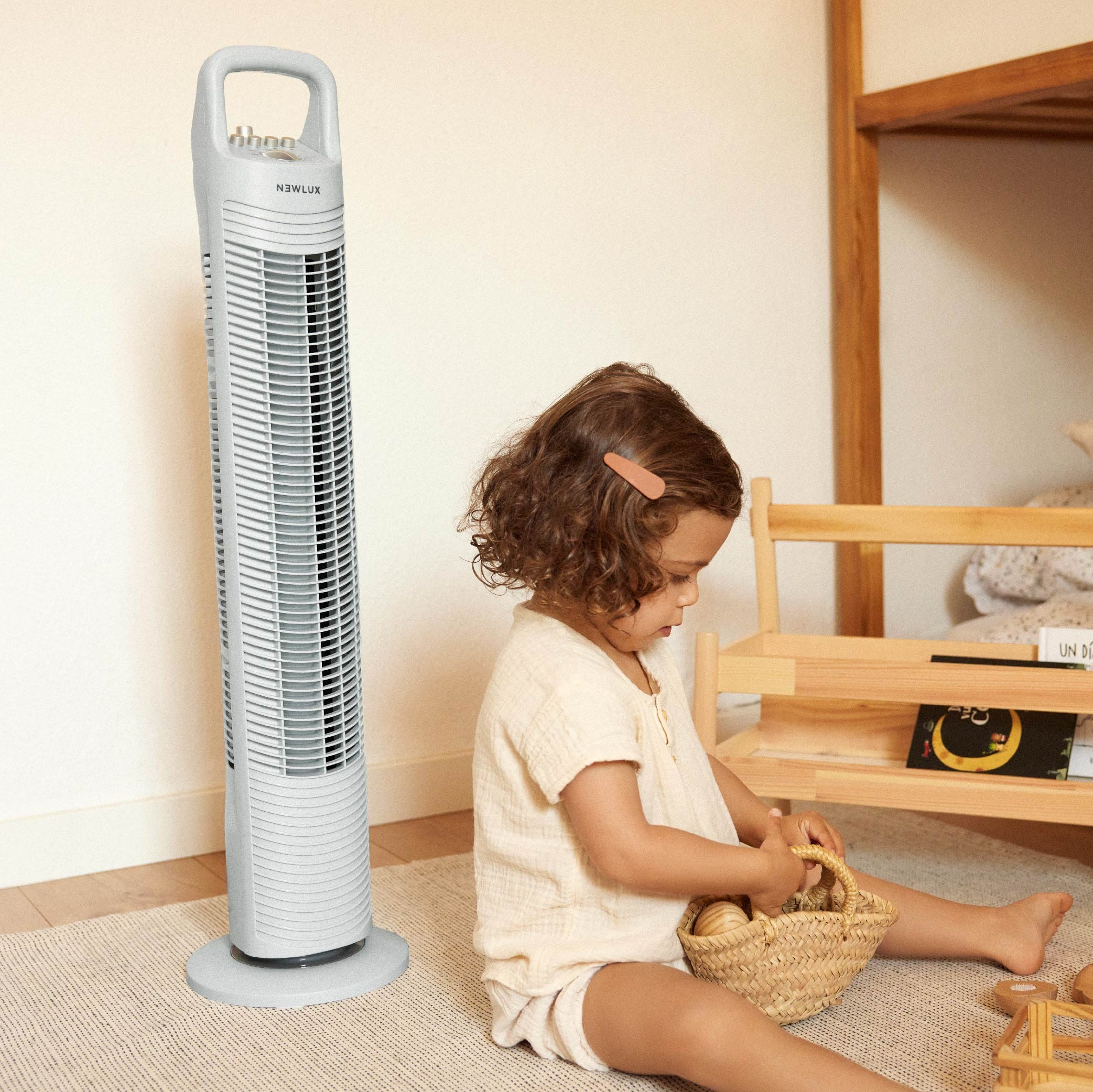 Una niña sentada cerca de un ventilador de torre y una estantería de madera con huevos.