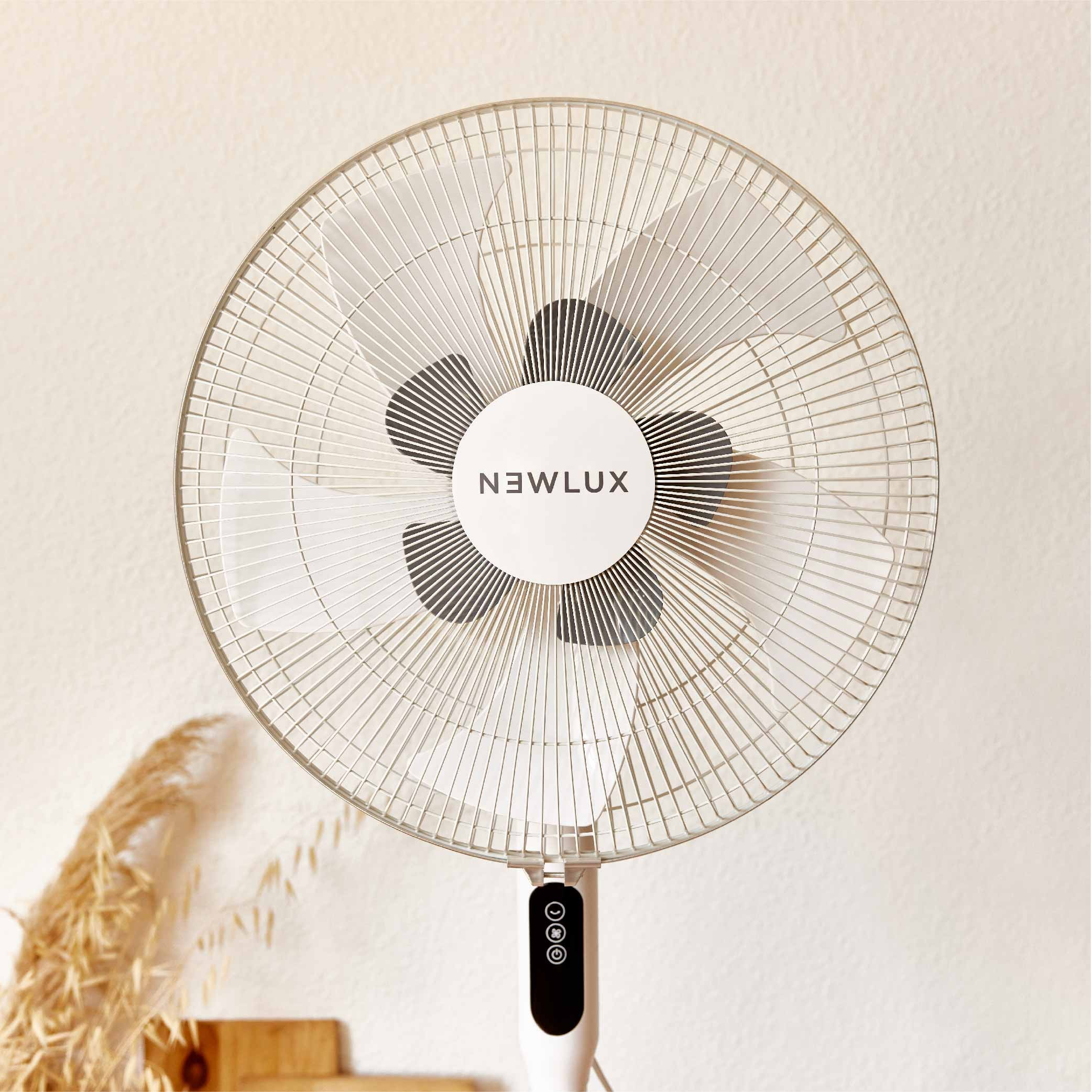 Ventilador Newlux blanco con cabezal redondo y tres aspas. Pared beige al fondo.