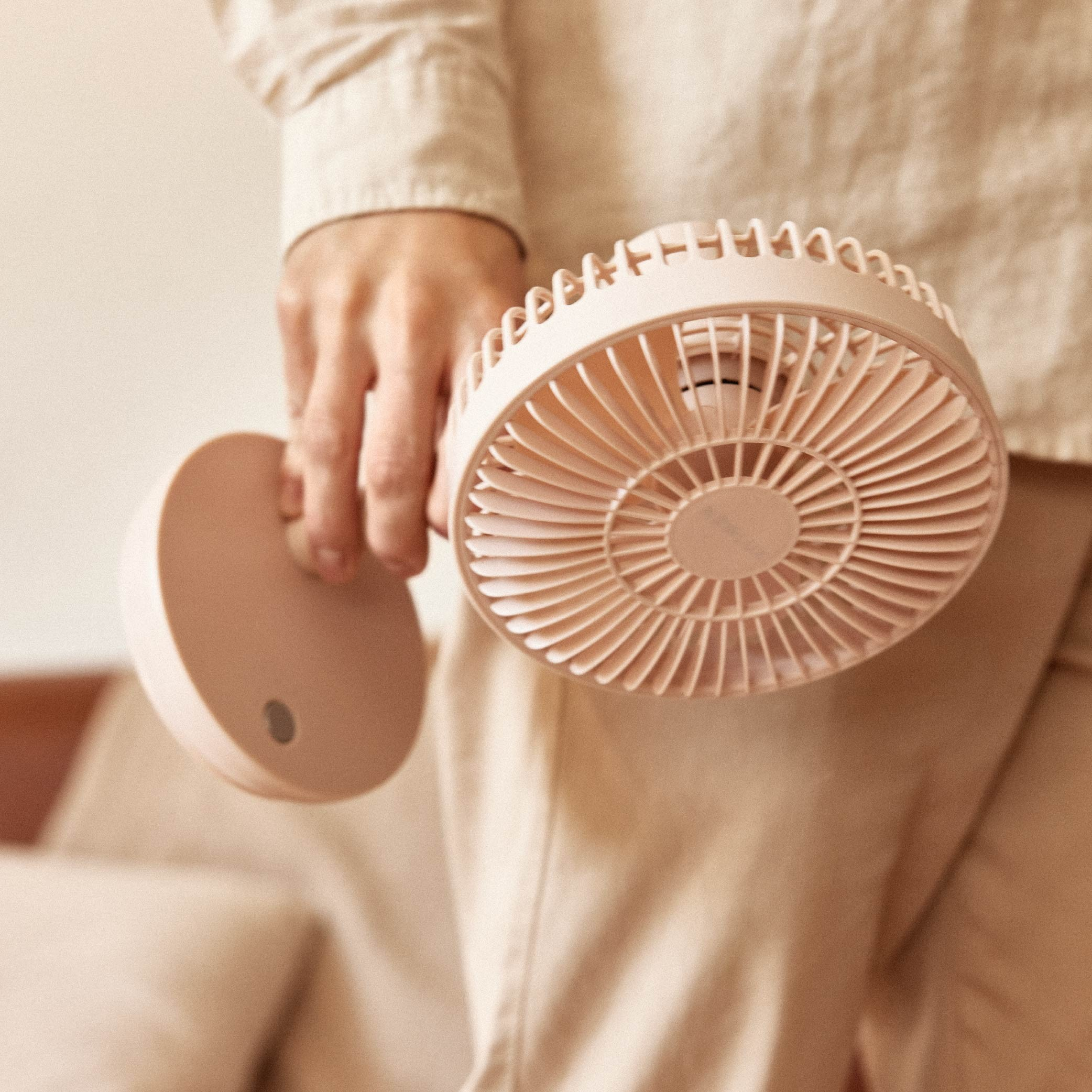 Persona sosteniendo un mini ventilador rosa. El ventilador es redondo, con soporte. Fondo beige.