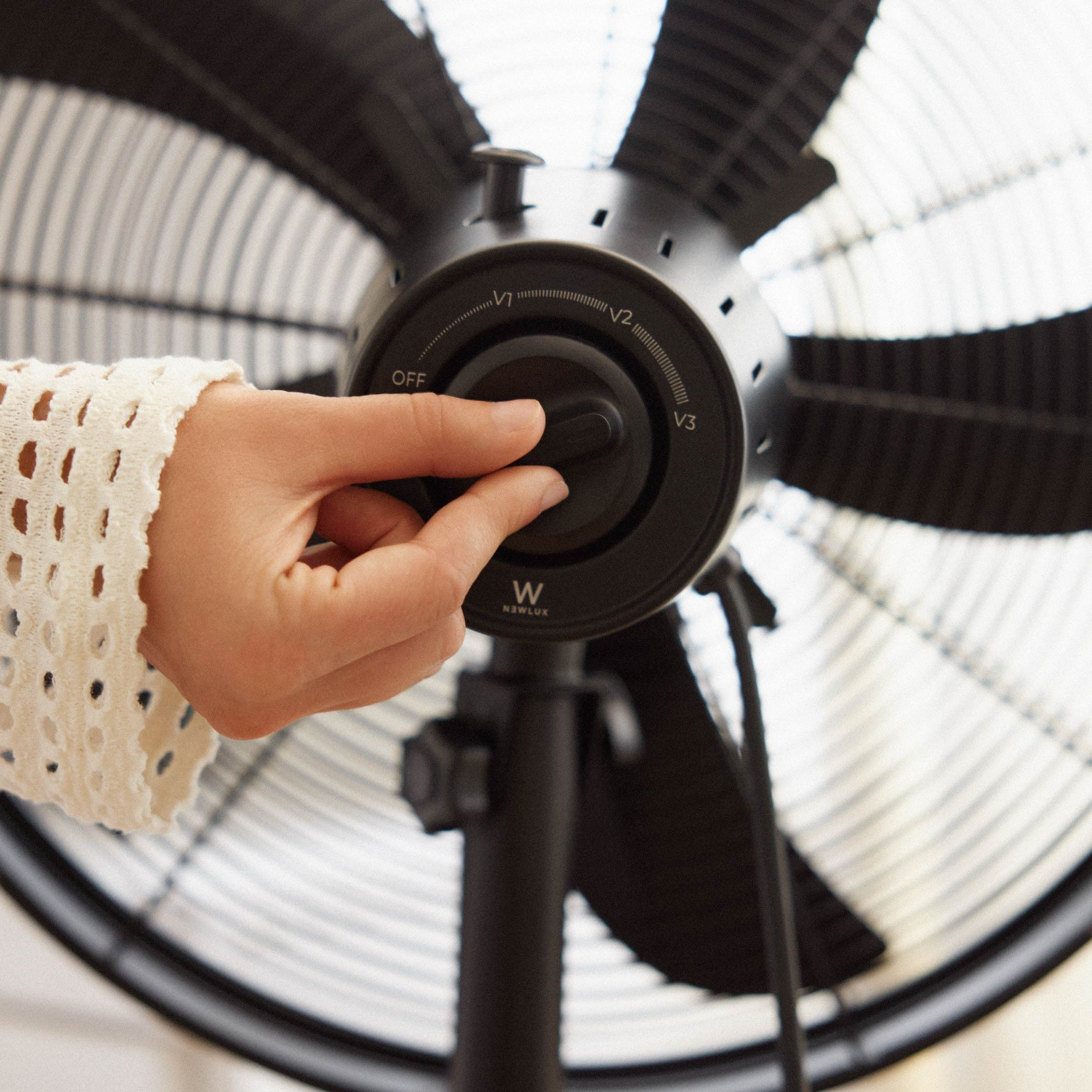 Mano de una persona ajustando el dial de velocidad en un ventilador de pie negro.