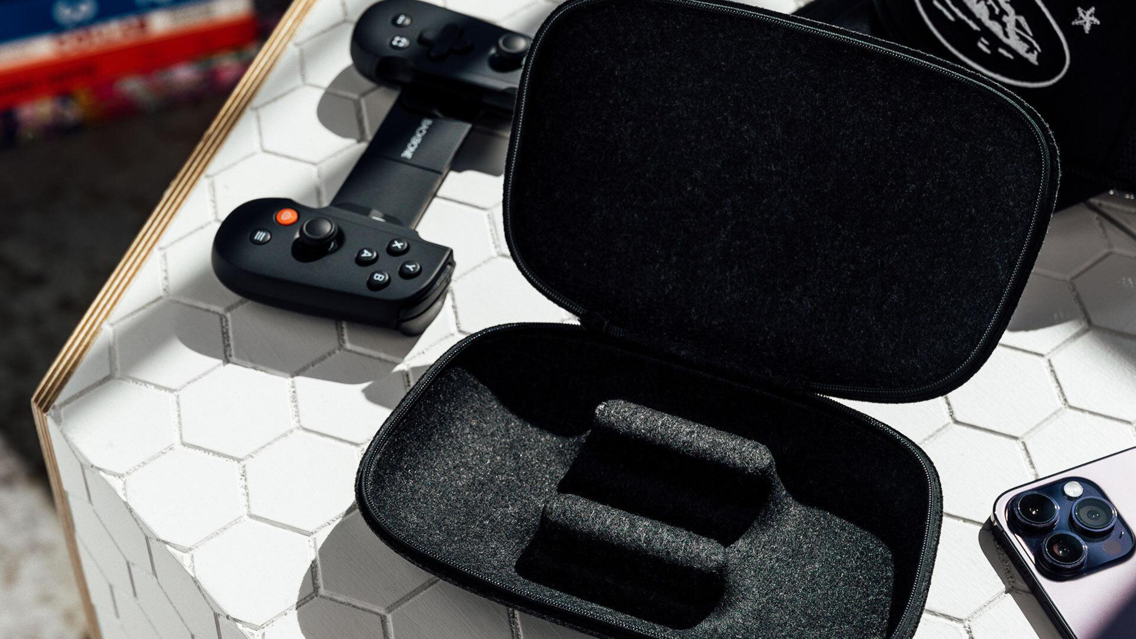 Controller di gioco nero e la sua custodia. Uno smartphone e altri oggetti sono sul tavolo.