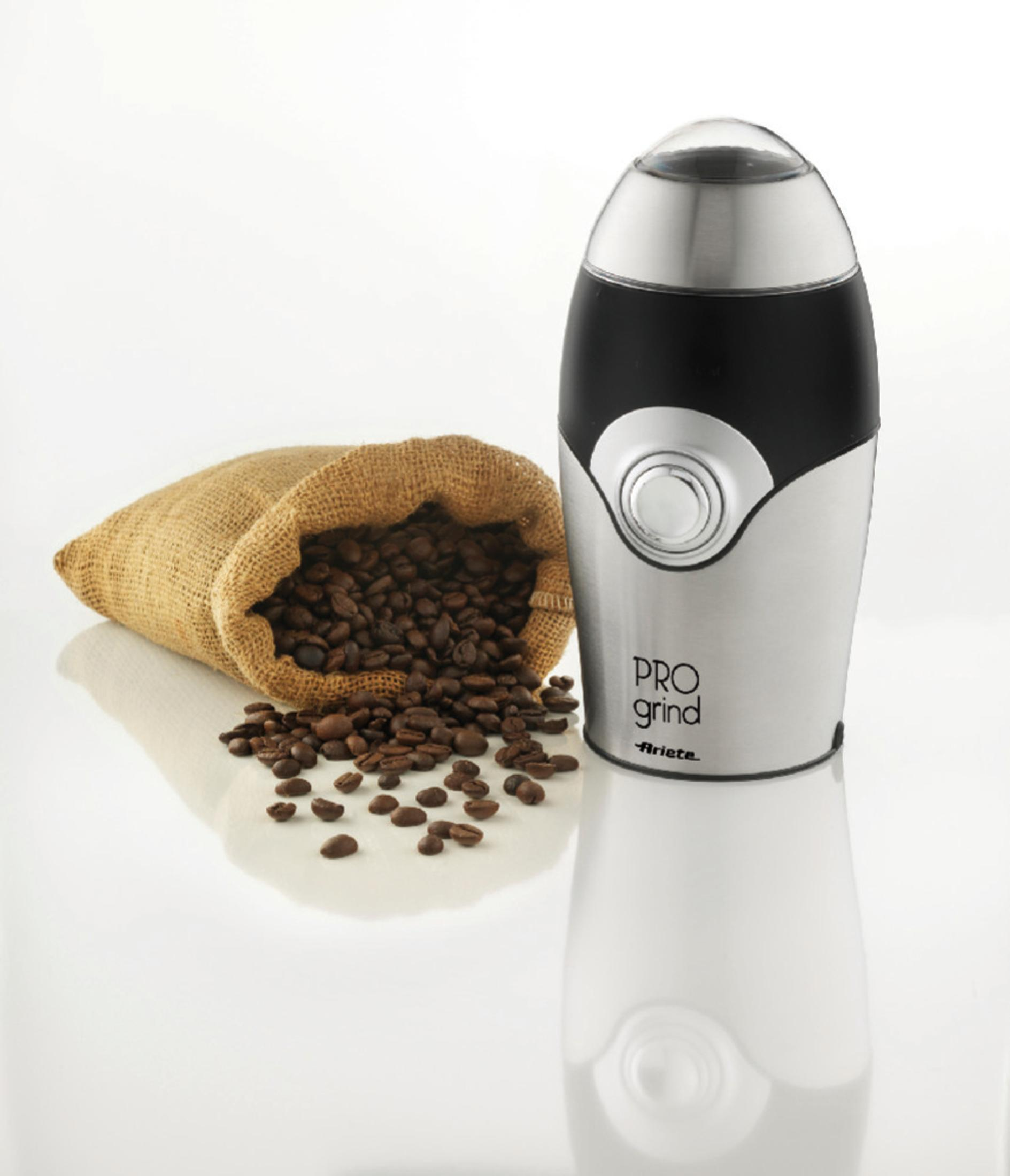 Kaffeebohnen in einem Jutesack neben einer silbernen und schwarzen Kaffeemühle.