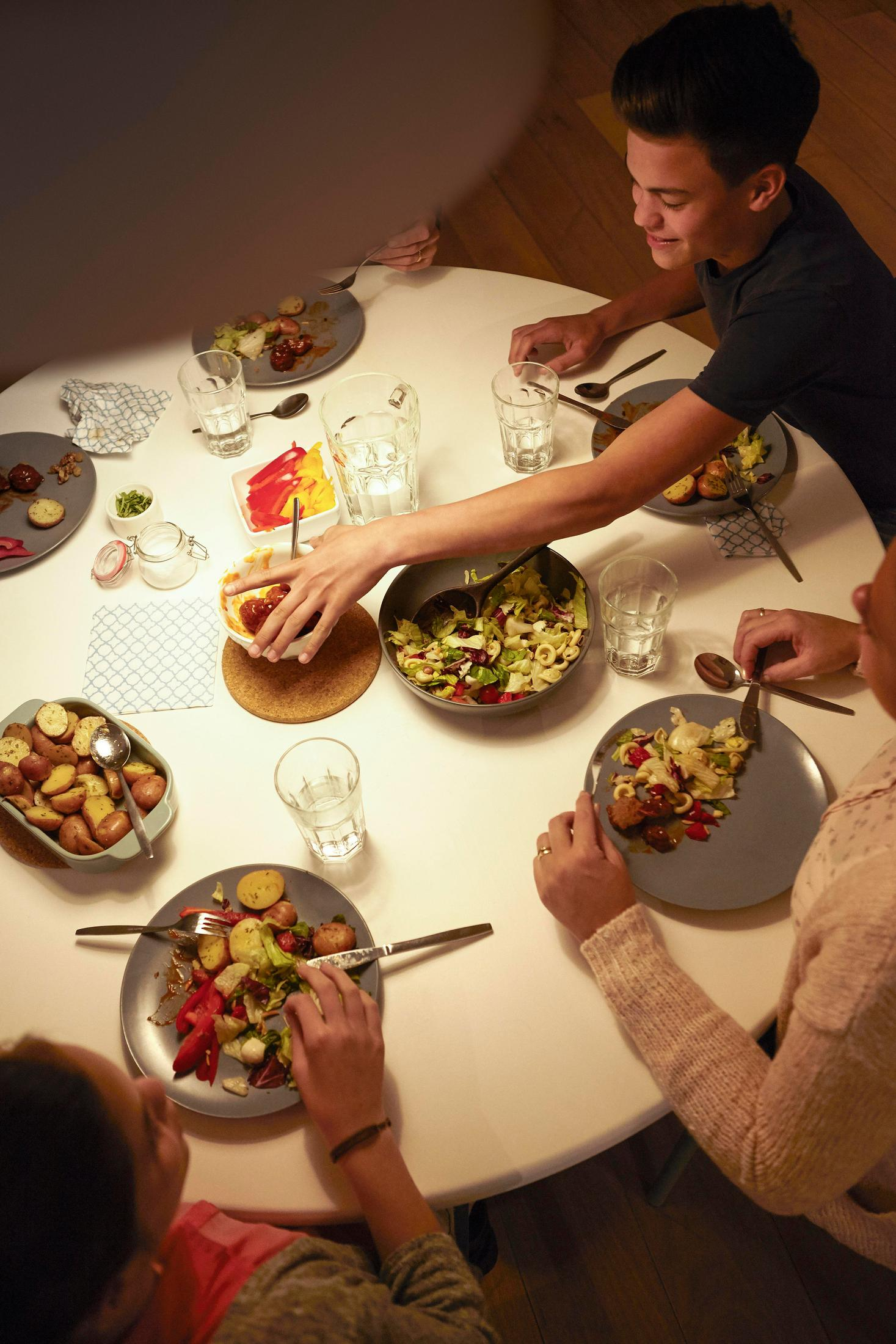 Des personnes mangent à une table ronde, avec des assiettes de nourriture, vue d'en haut.