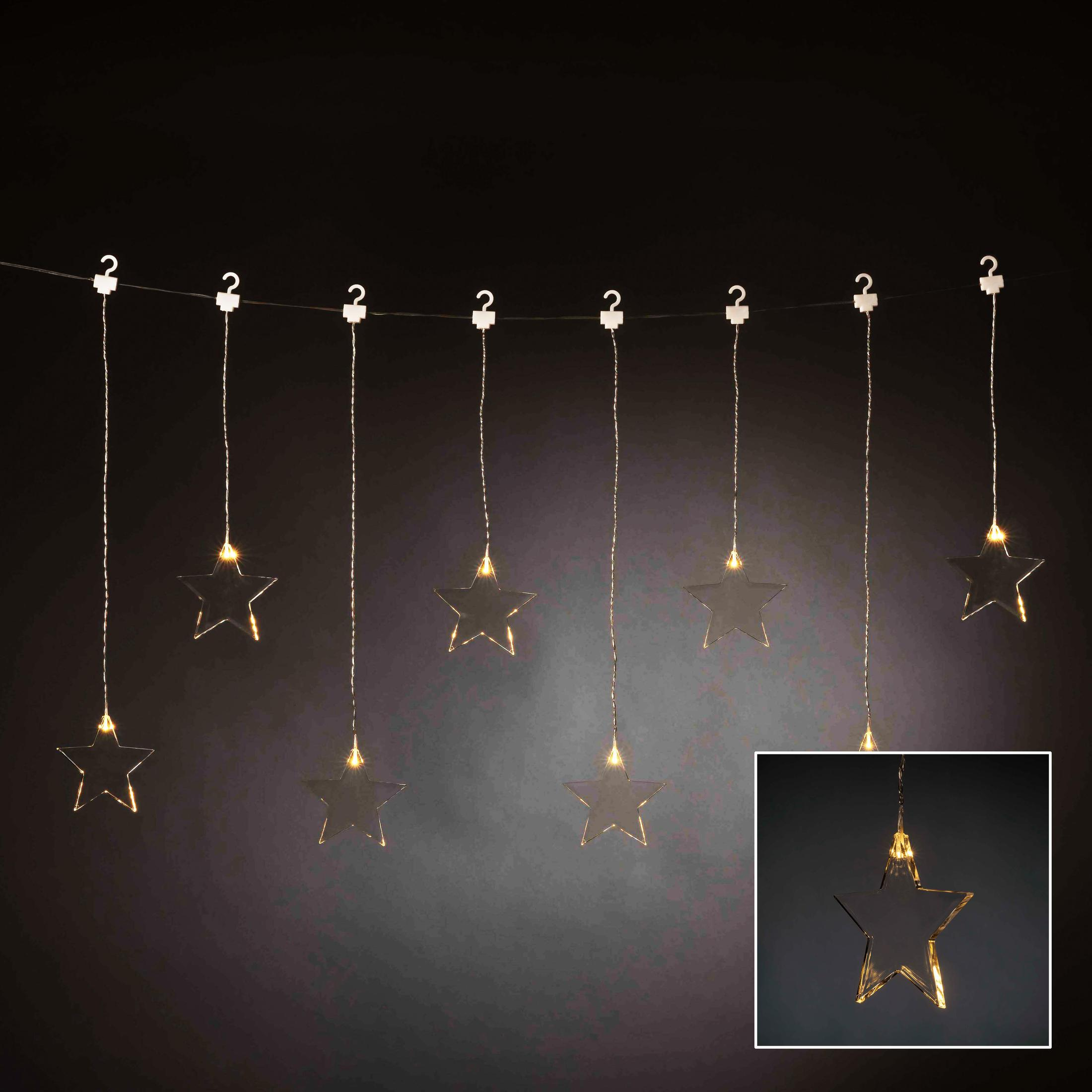 Lichterkette mit Sternformen, die an einem Draht hängen. Die Sterne leuchten warm vor dunklem Hintergrund.