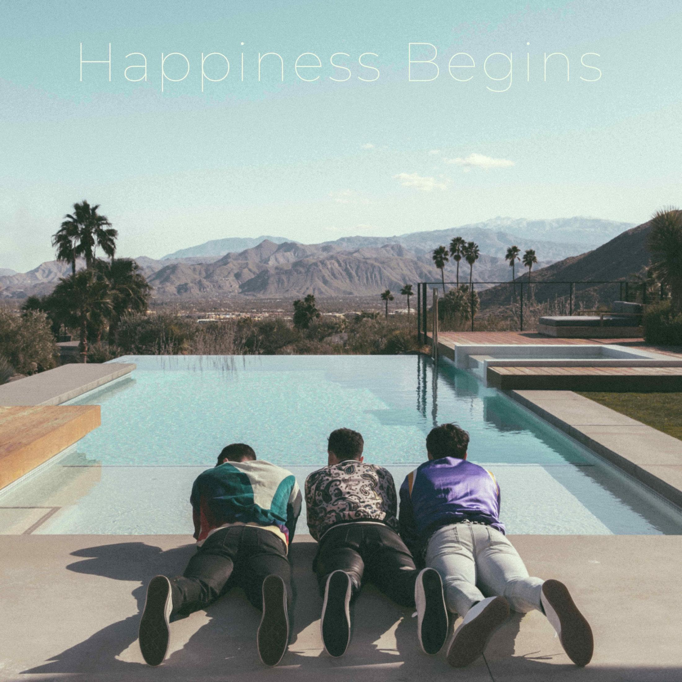 Tre uomini sdraiati a bordo piscina, affacciati sulle montagne. Testo "Happiness Begins".