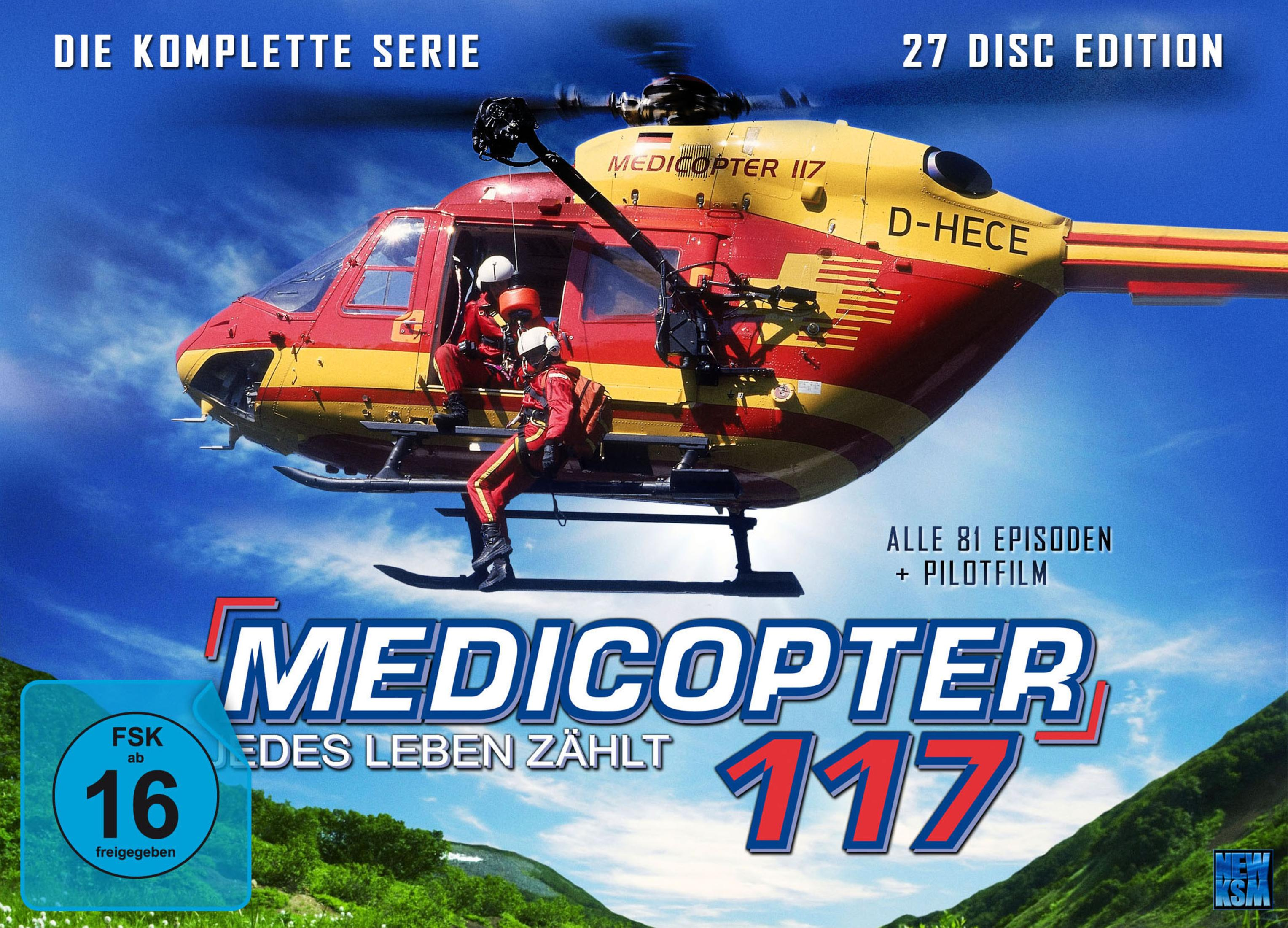 Un hélicoptère de sauvetage rouge et jaune vole dans le ciel bleu. Deux personnes en combinaison rouge sont visibles.