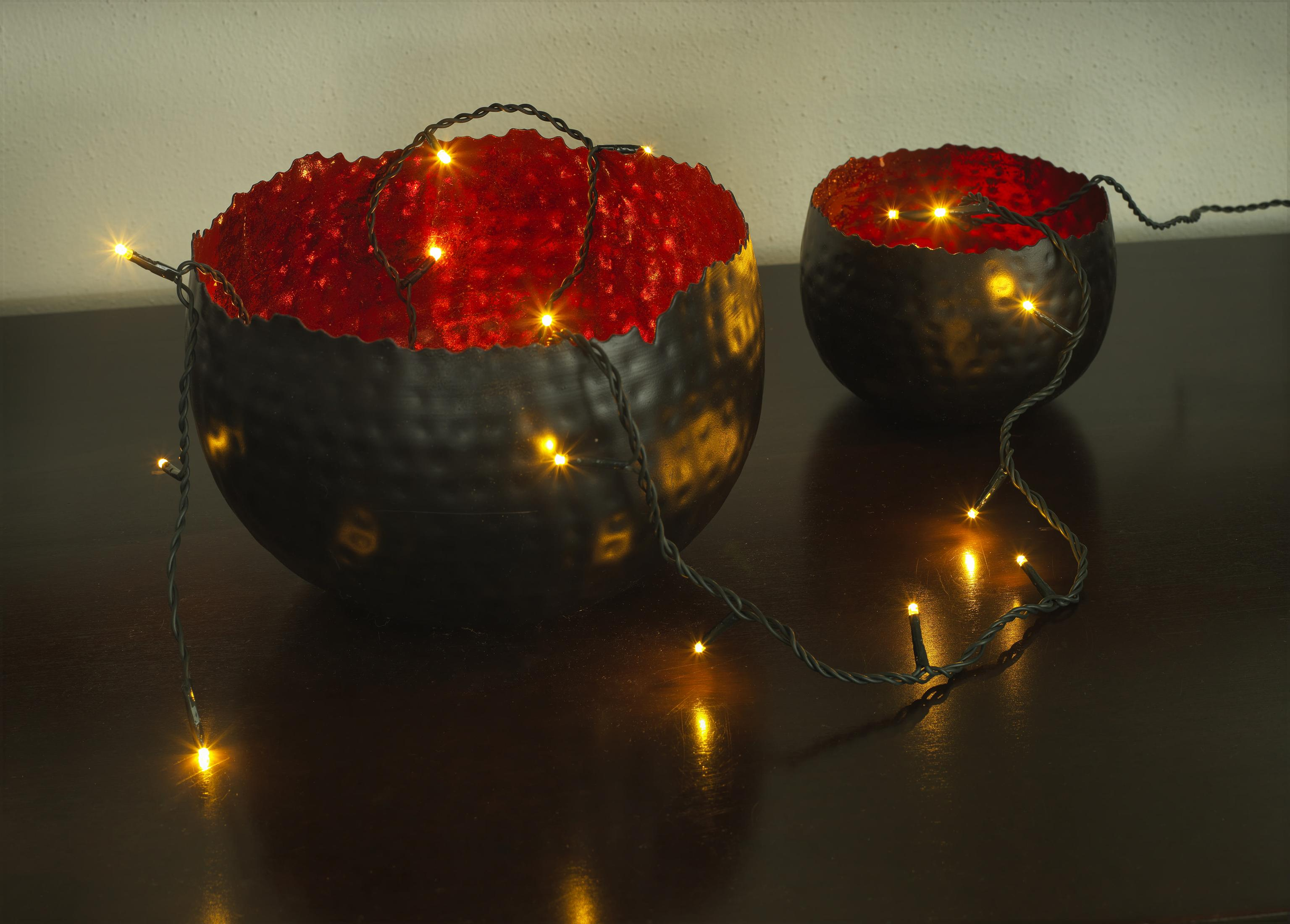 Zwei schwarze Schalen mit roten Innenräumen, Lichter, auf einer Holzoberfläche. Die Szene ist warm und einladend.