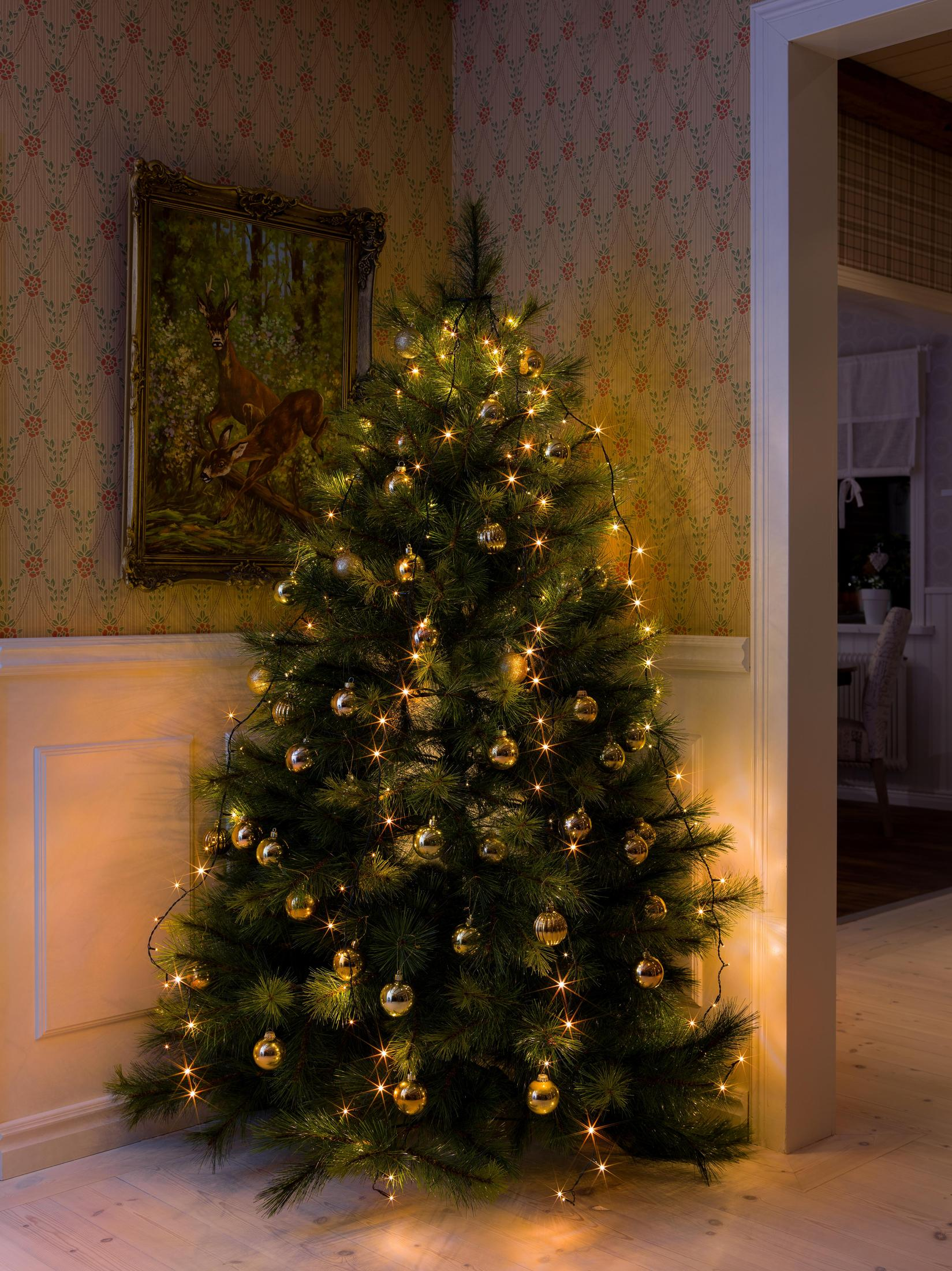 Ein geschmückter Weihnachtsbaum in einem Raum mit einem Gemälde. Er hat Lichter und goldene Ornamente.