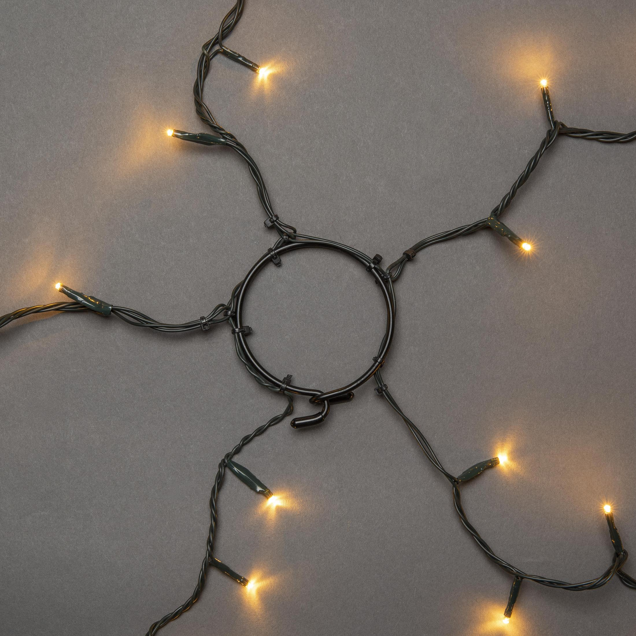 Ein Ring aus Weihnachtslichtern mit grüner Verkabelung, vor grauem Hintergrund.