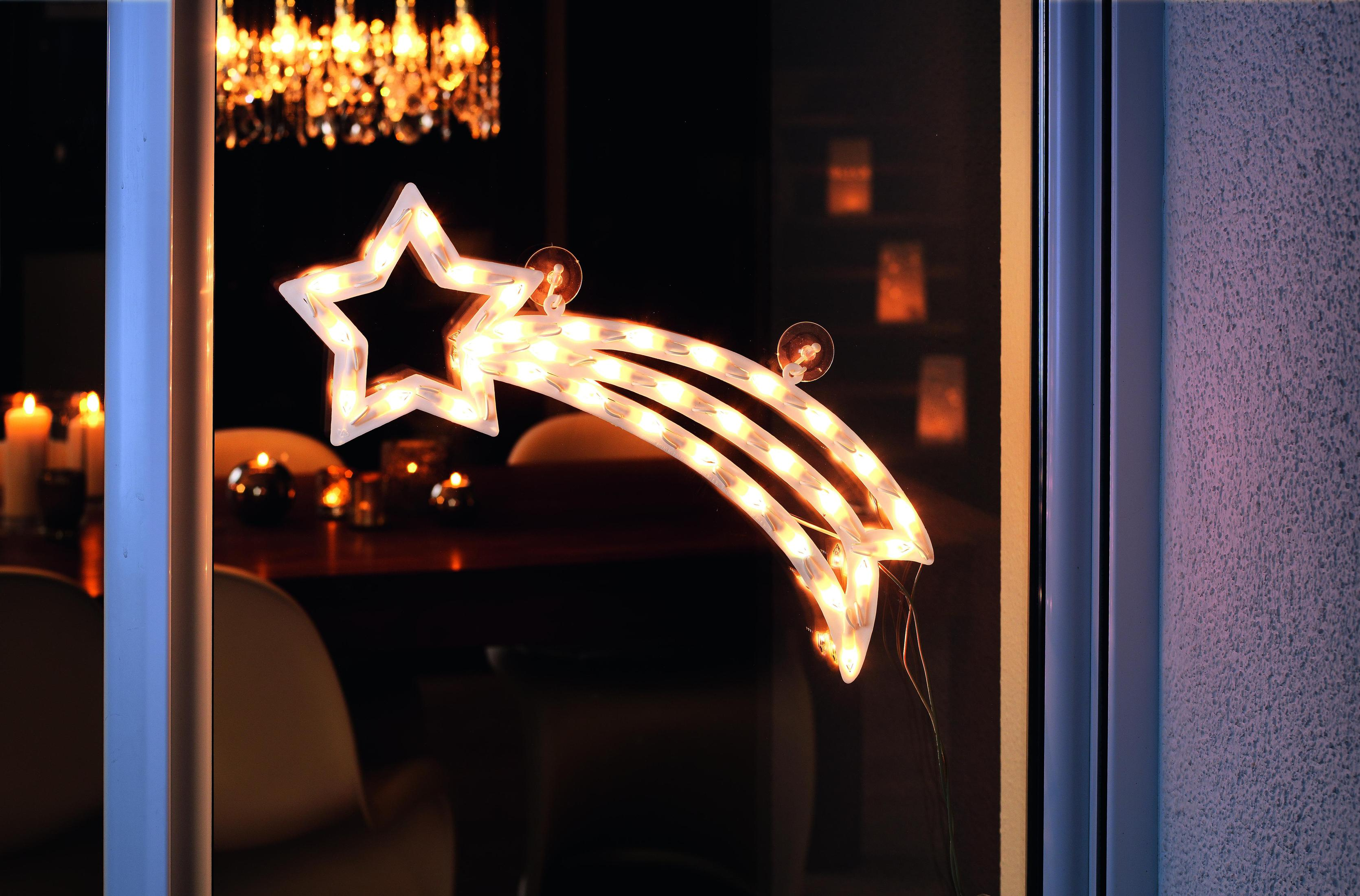 Una finestra con una decorazione luminosa a forma di stella, che riflette un interno con candele.