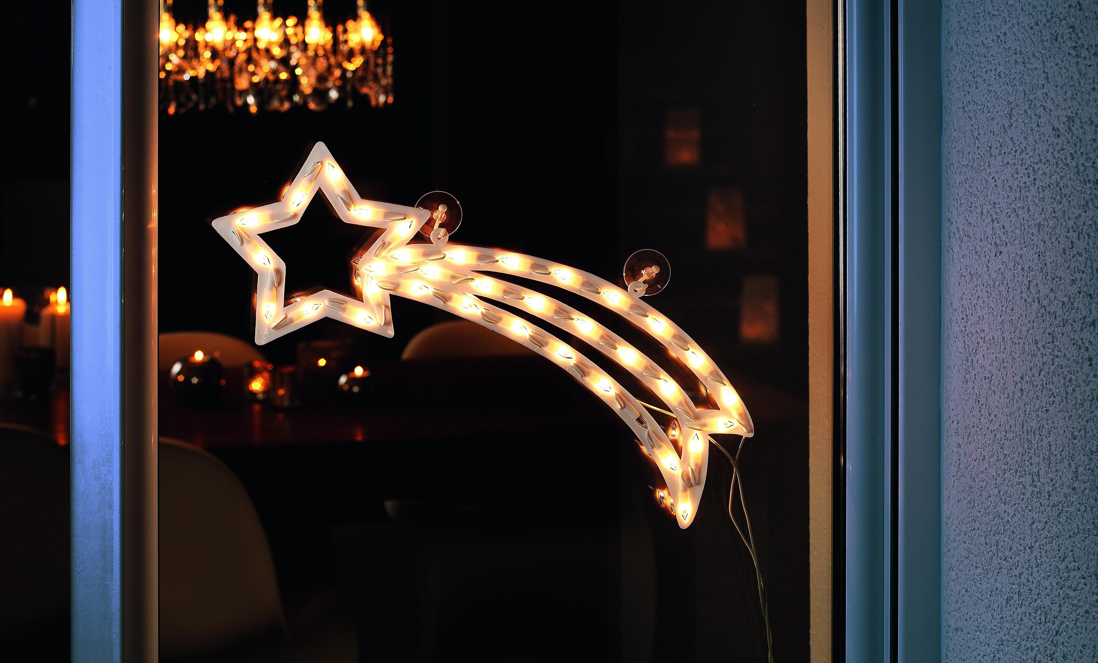 Decorazione natalizia a forma di stella illuminata su una finestra. Interno sfocato con candele.