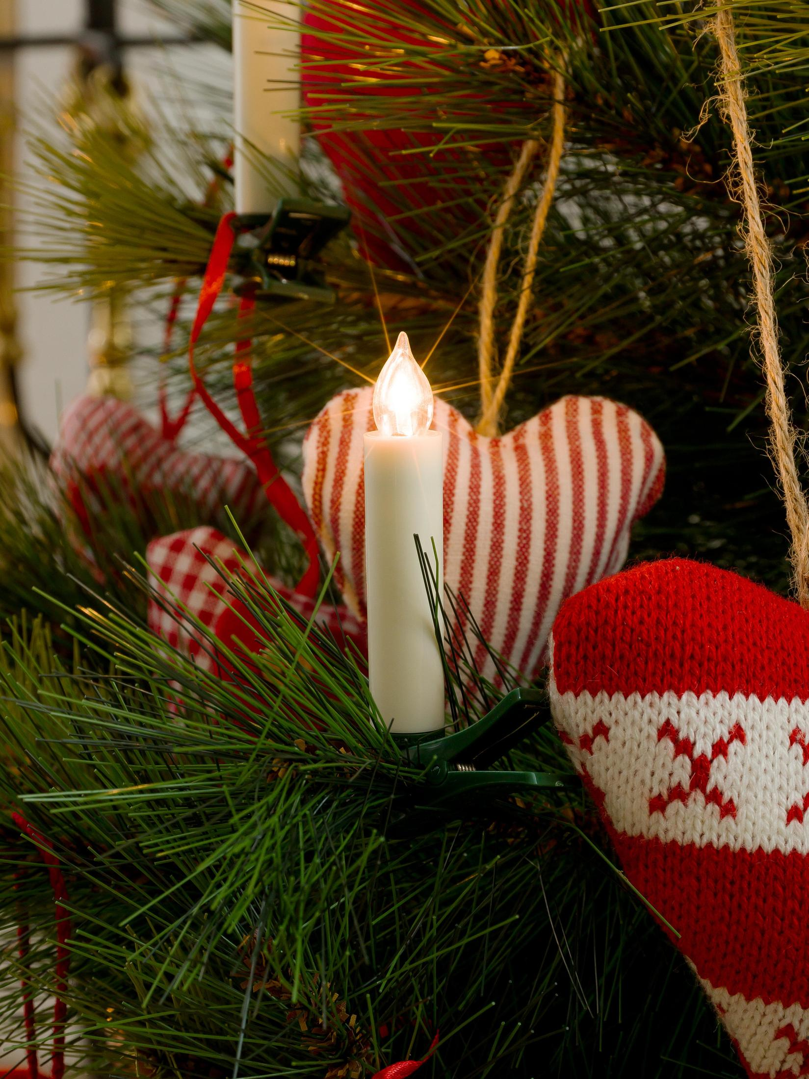 Nahaufnahme eines Weihnachtsbaumes mit Lichtern und Ornamenten. Eine brennende Kerze steht im Zentrum.