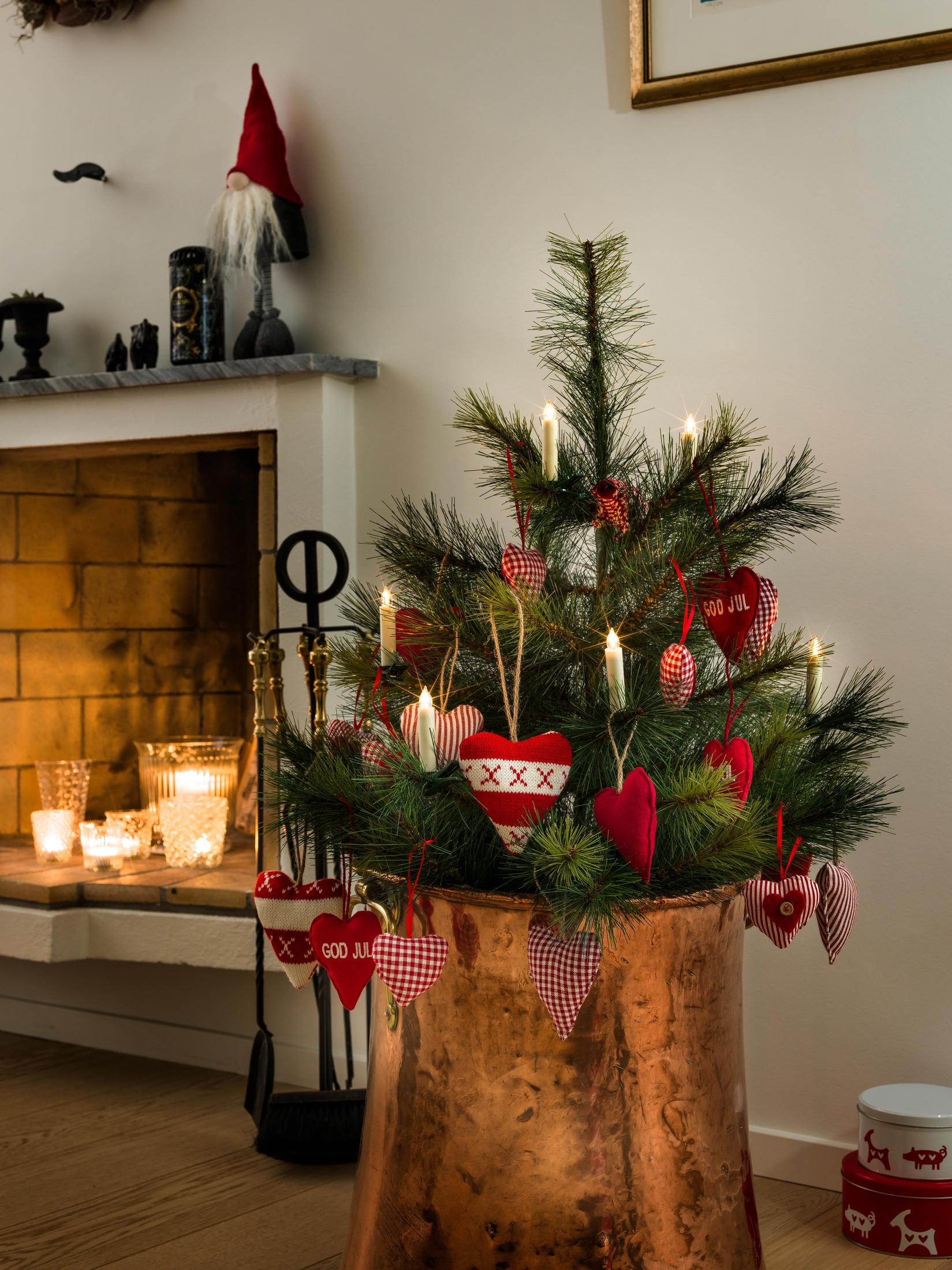 Ein Weihnachtsbaum mit Herzschmuck und brennenden Kerzen in einem Kupfertopf in einem Haus.