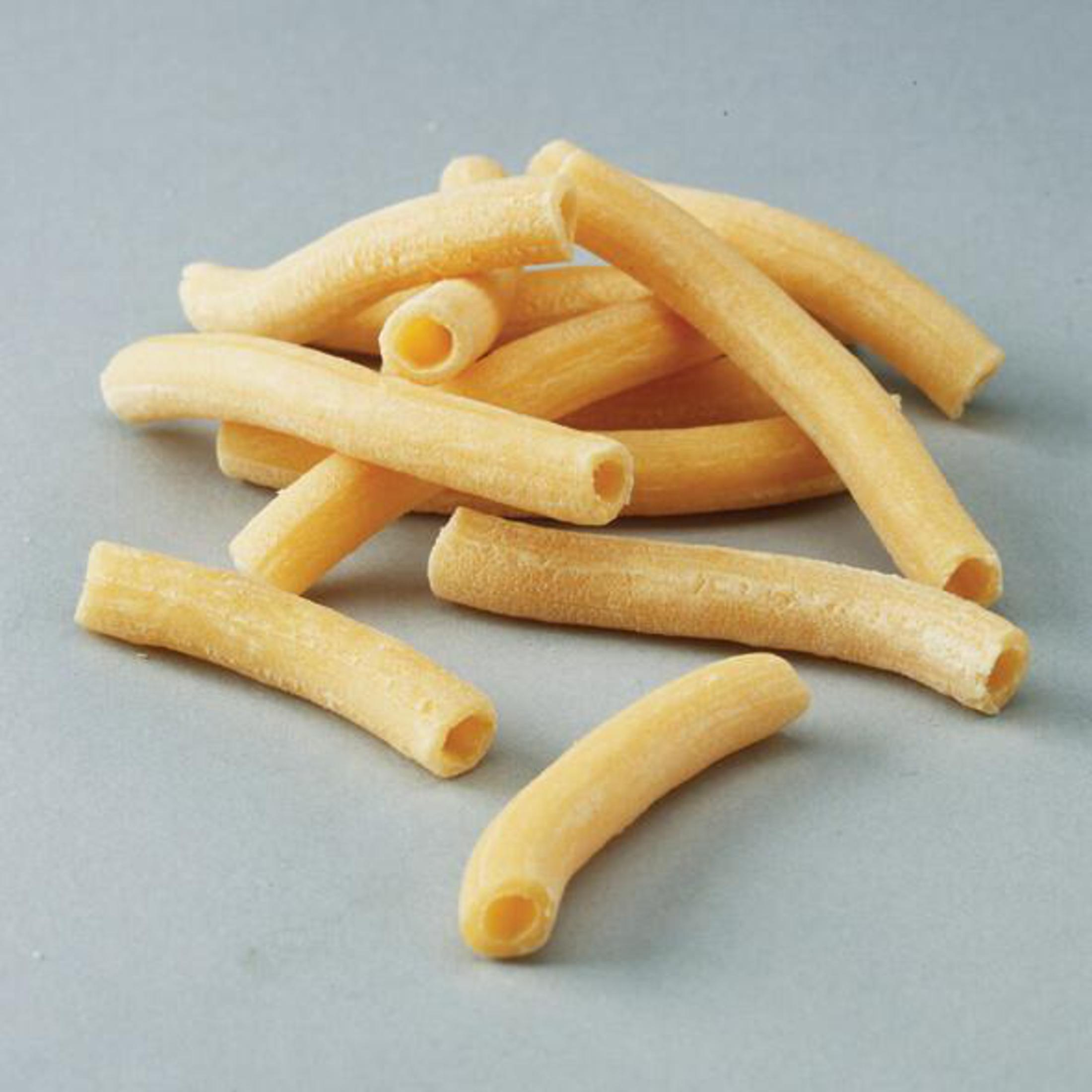Pâtes jaunes en forme de tubes courts. Les pâtes sont sur une surface grise.