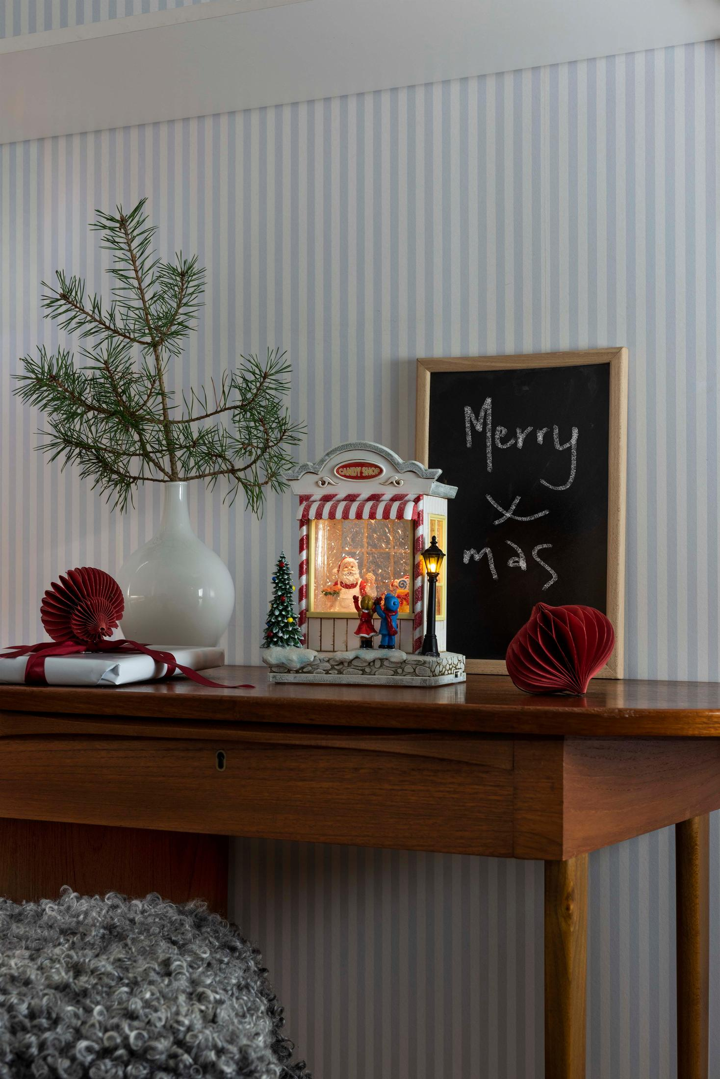 Un tavolo decorato con una scena natalizia, un albero e una lavagna con scritto 'Merry Xmas'.