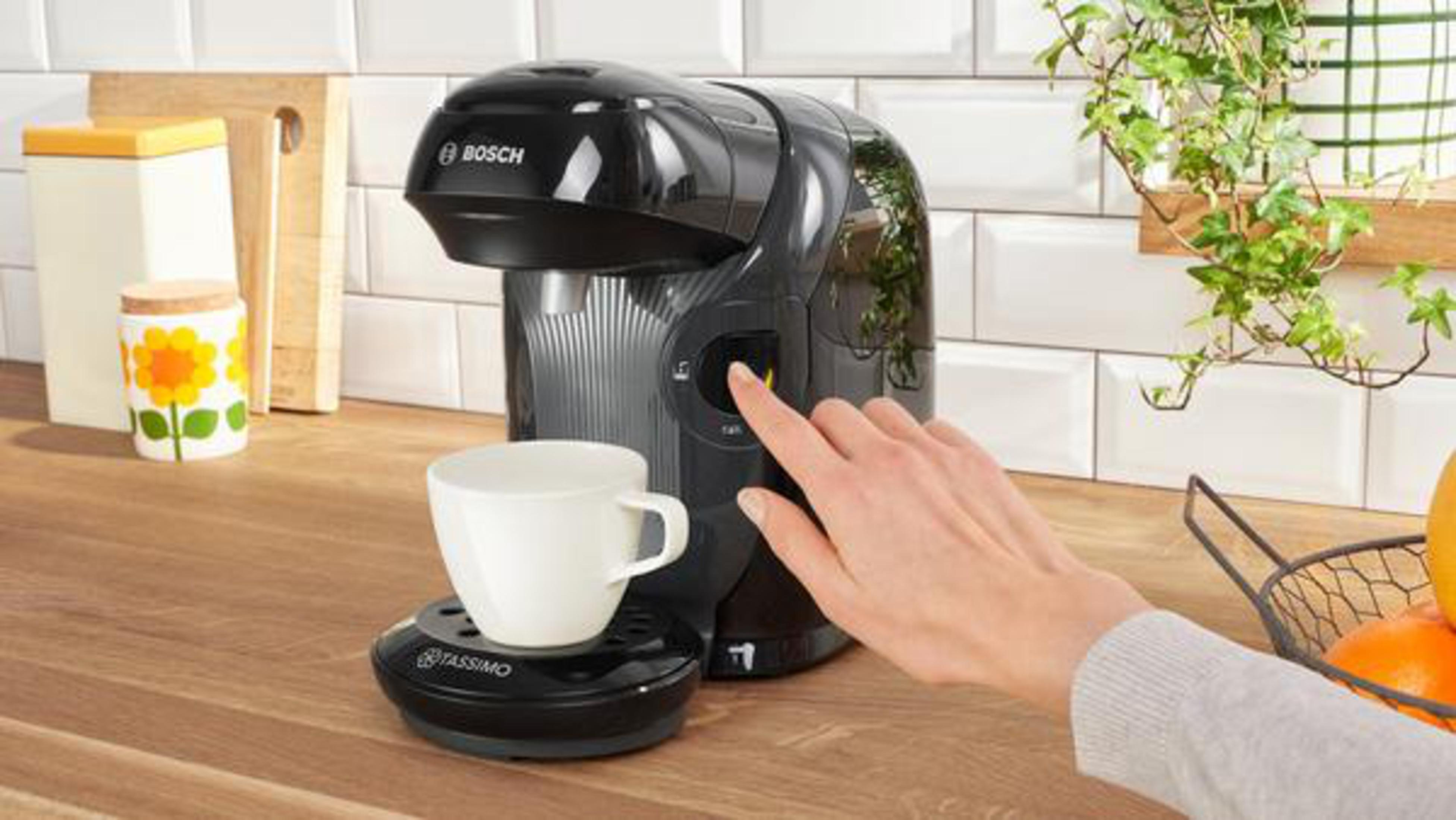 Donna che fa il caffè con macchina Tassimo Bosch nera. Tazza bianca.