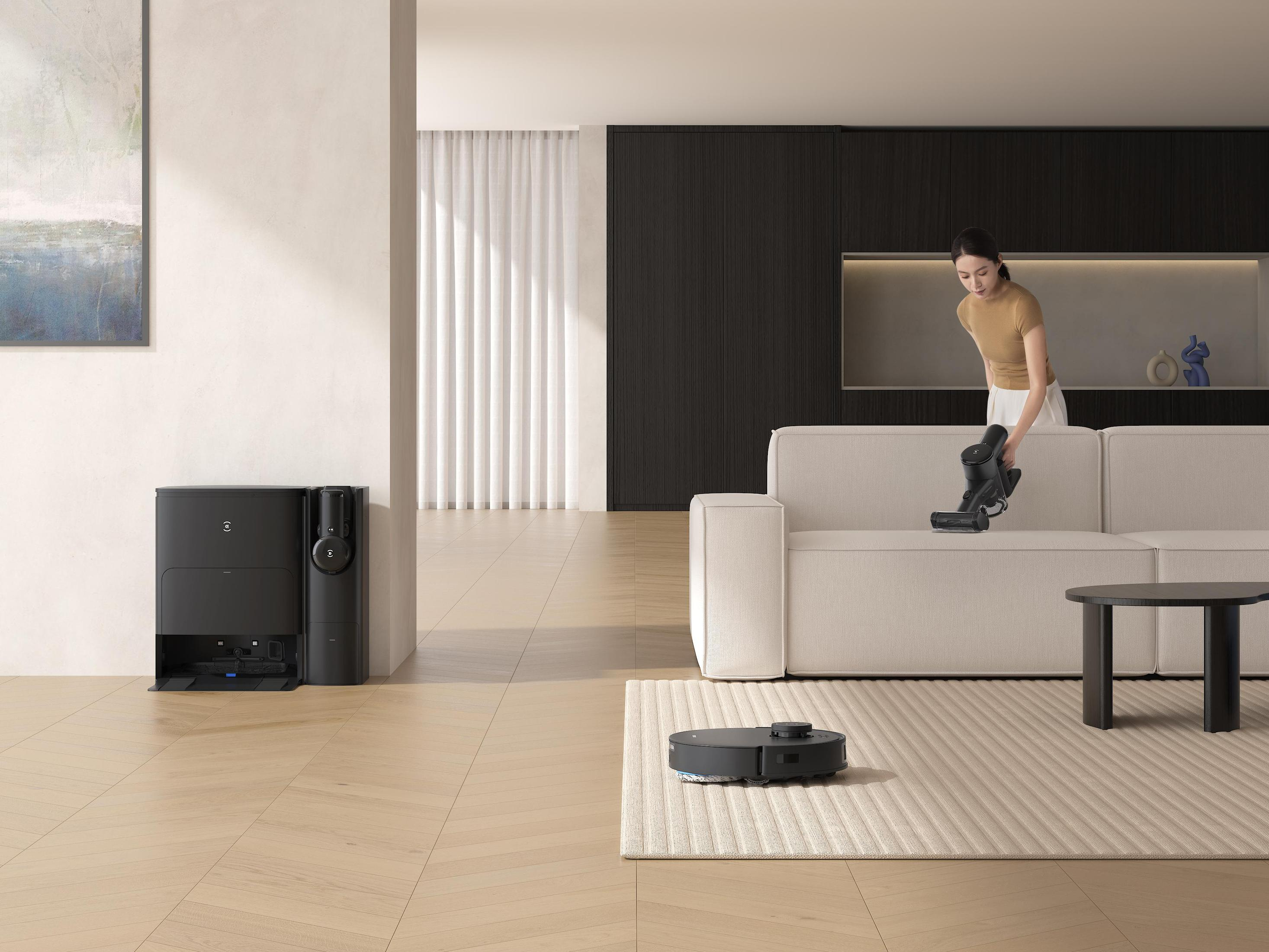 Kobieta odkurza sofę w nowoczesnym salonie z robotem sprzątającym.
