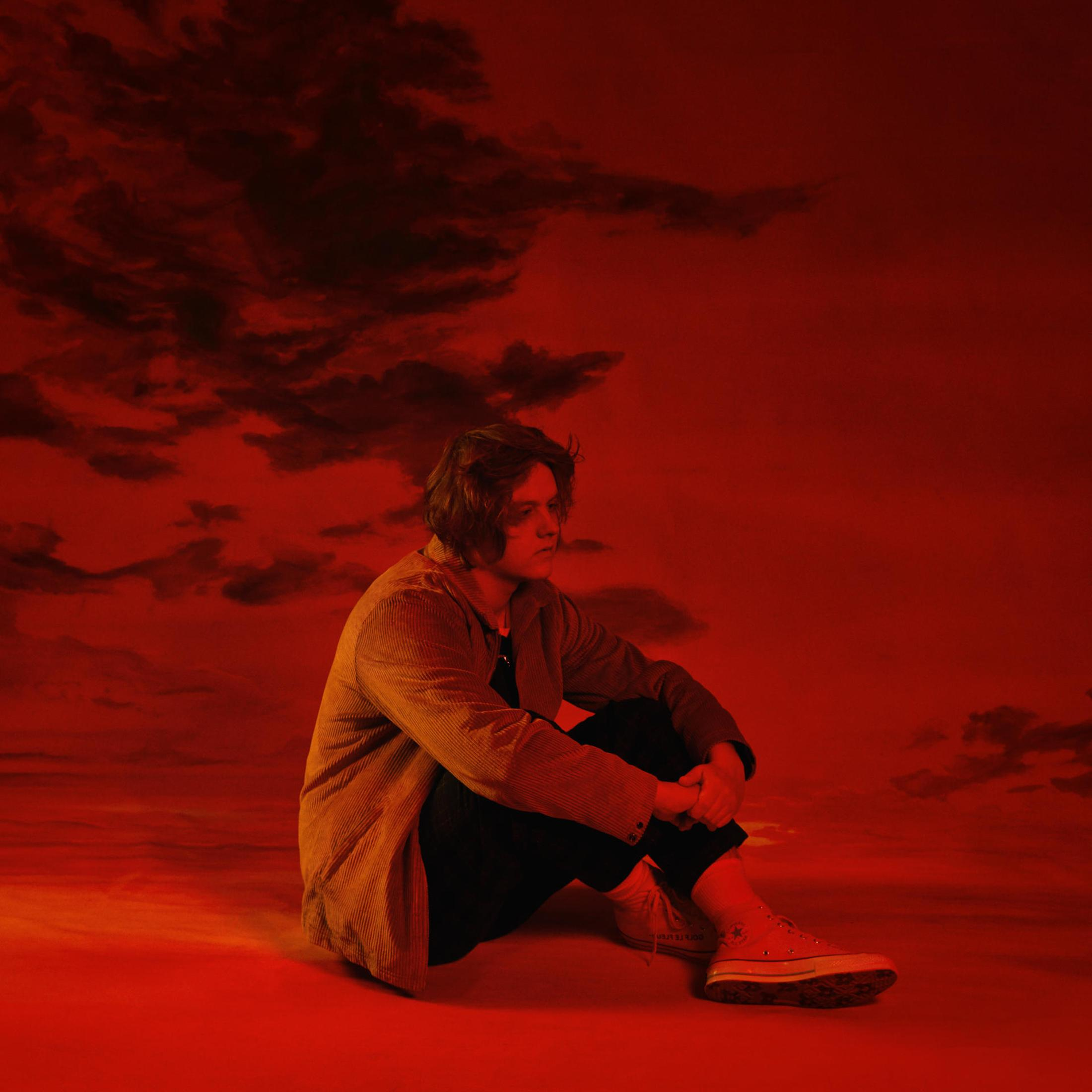 Albumhoes van Lewis Capaldi. Hij zit, kijkt naar beneden, met een rode, bewolkte lucht.