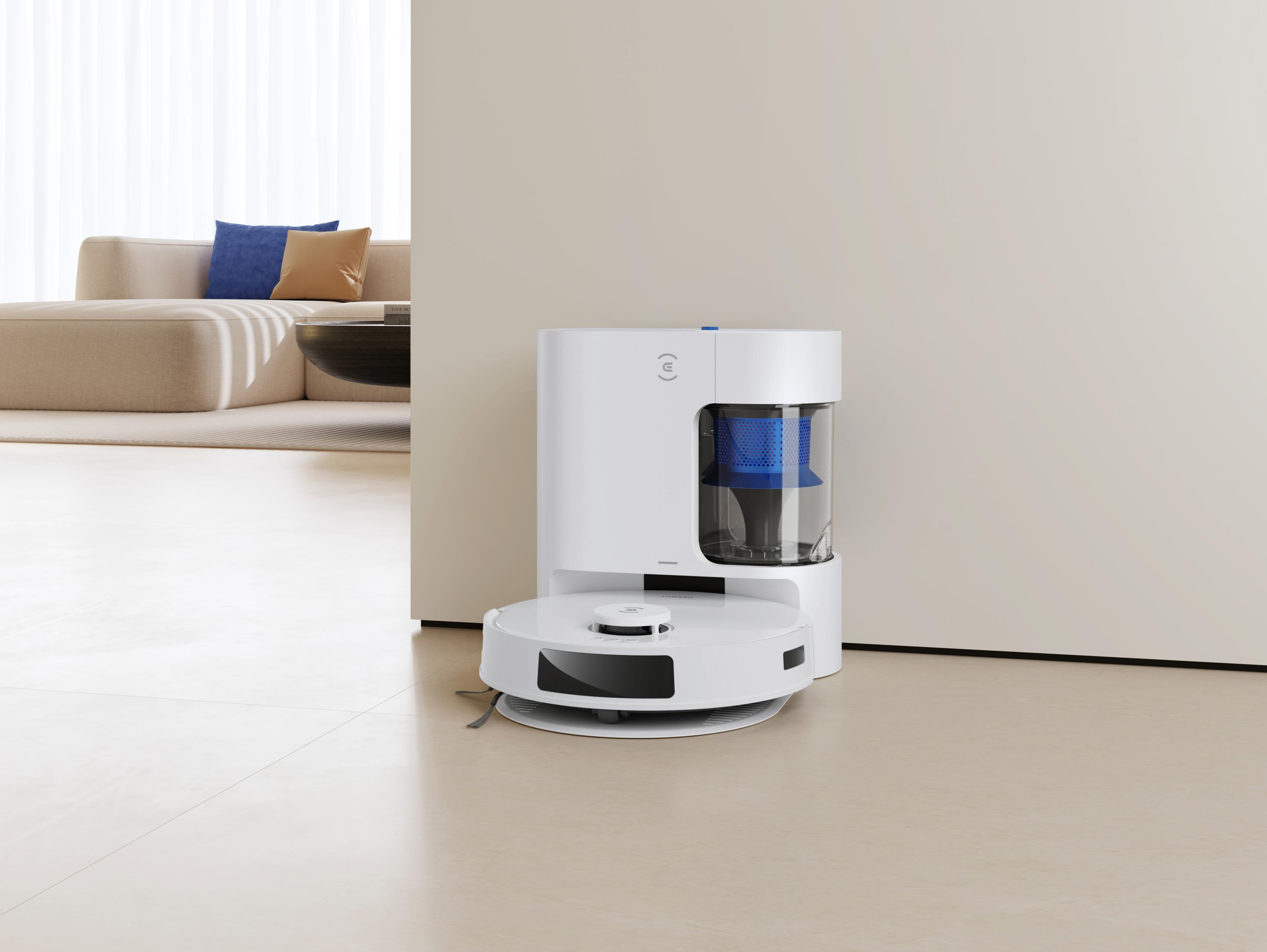 Biały odkurzacz automatyczny i jego stacja ładująca w pokoju z kanapą w tle.