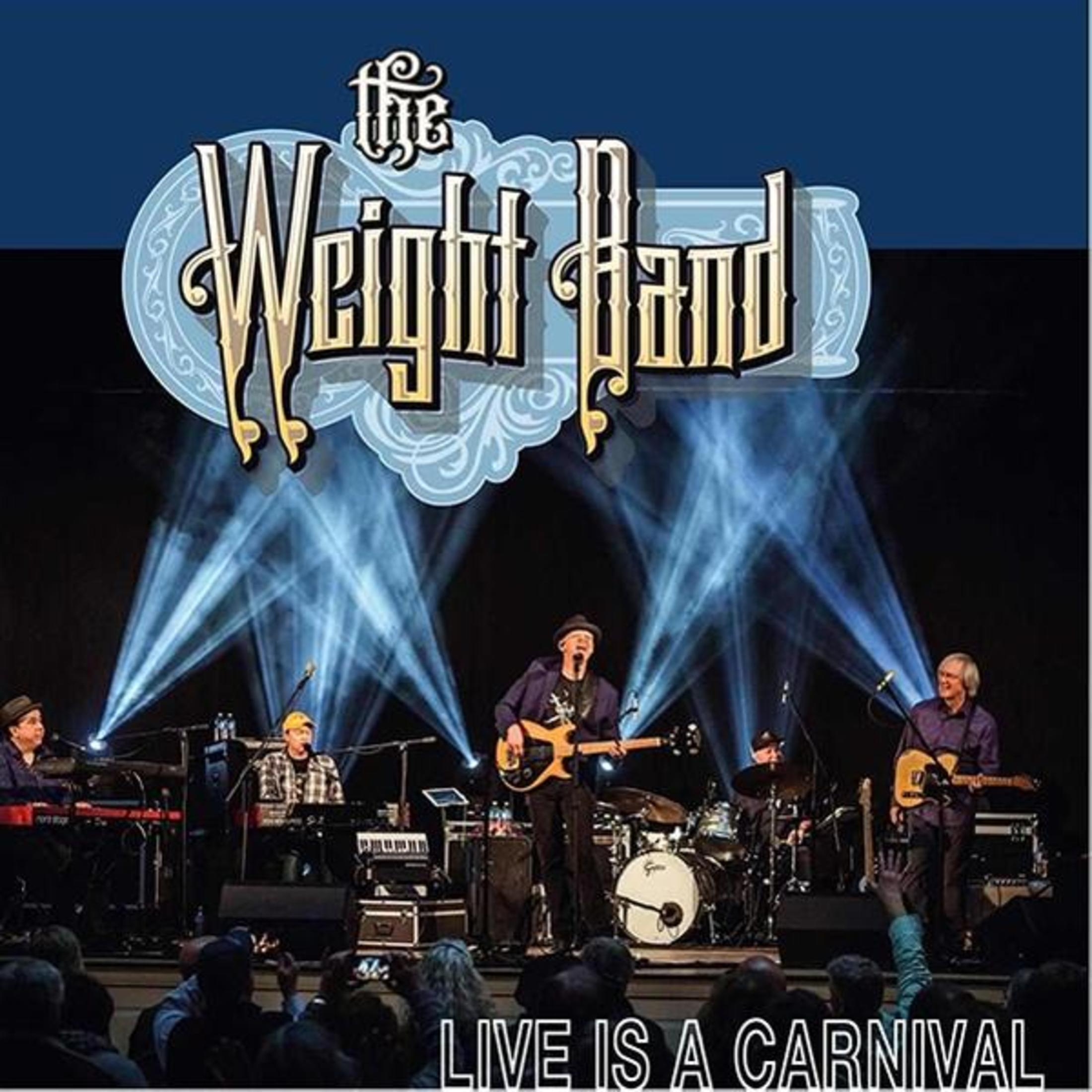 The Weight Band sur scène, fond bleu. Membres du groupe jouant des instruments, public au premier plan.