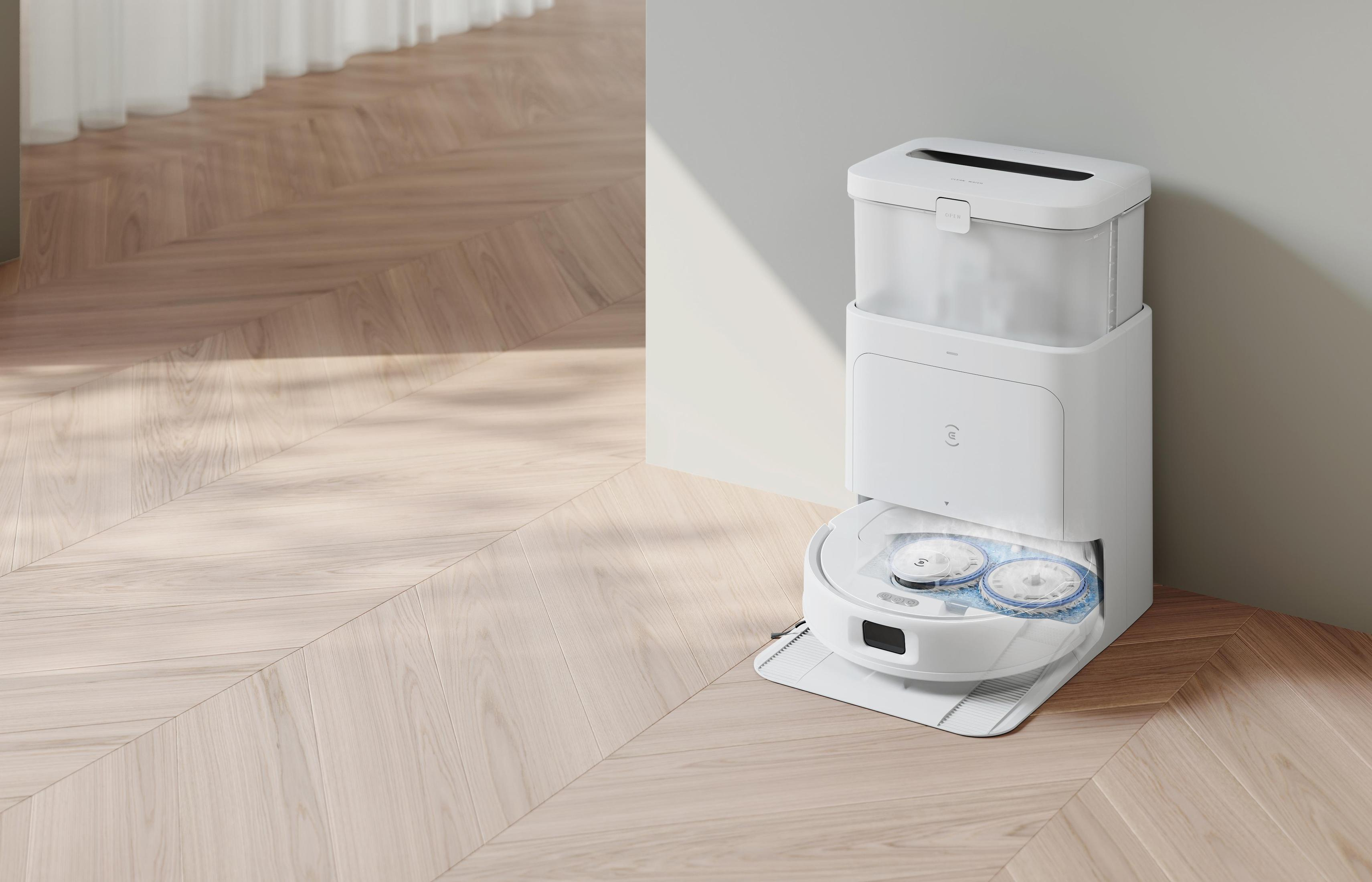 Biały robot odkurzający ze stacją ładującą na jasnej drewnianej podłodze.