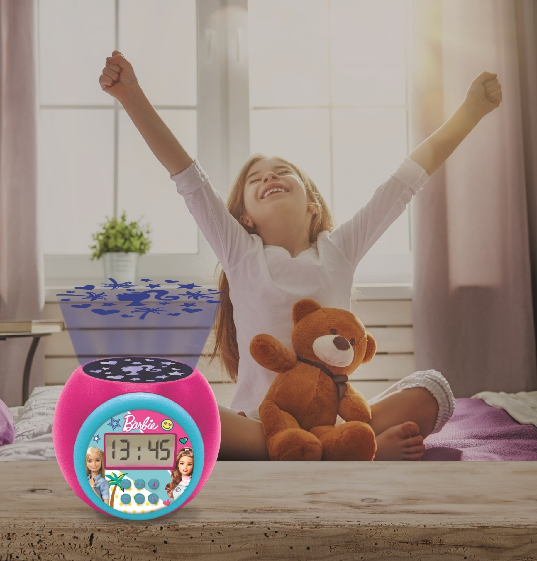 Un reloj Barbie rosa con una niña sonriendo. Un oso de peluche junto al reloj.