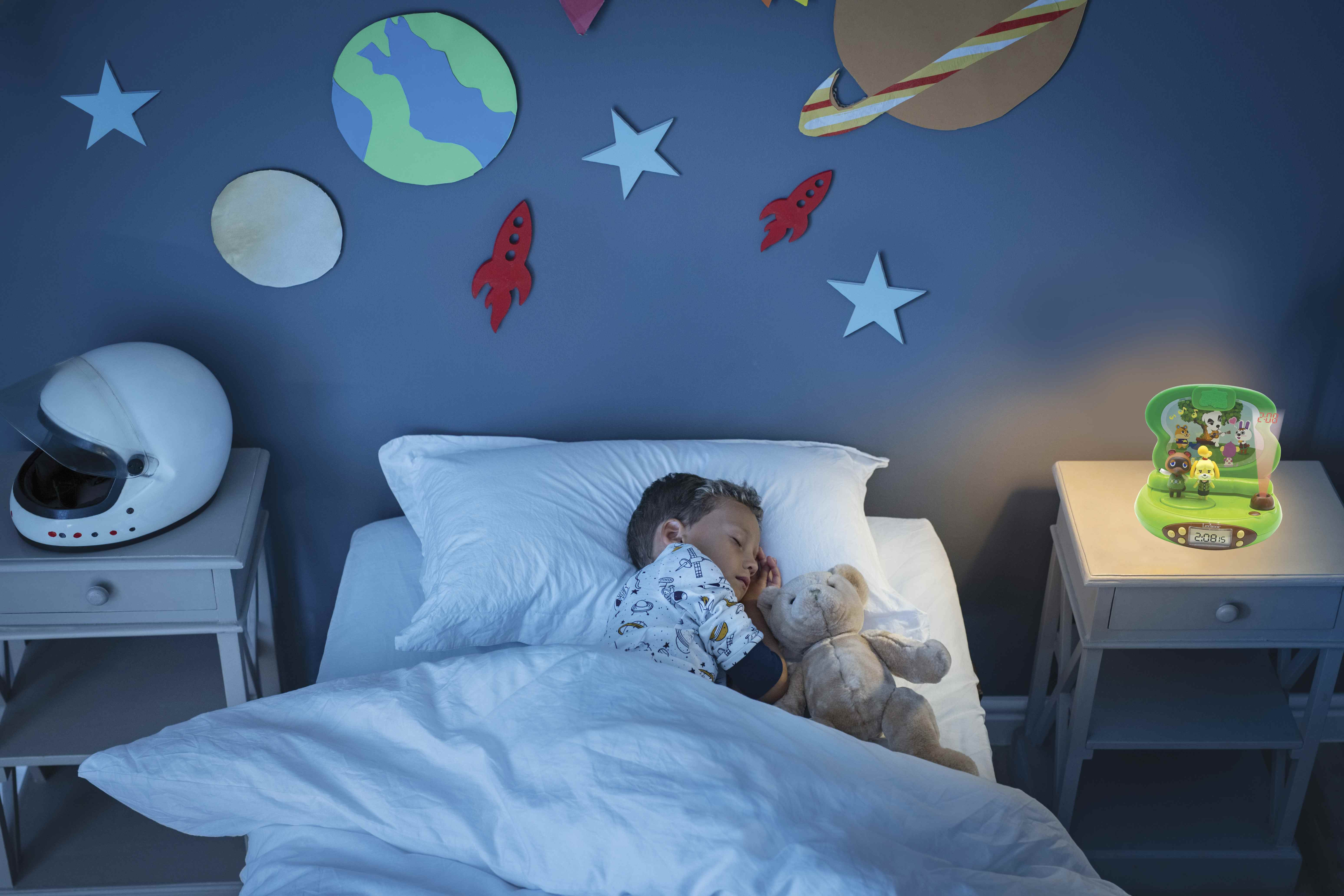 Un bambino che dorme a letto con un giocattolo, una luce notturna con personaggi dei cartoni animati e un muro a tema spaziale.